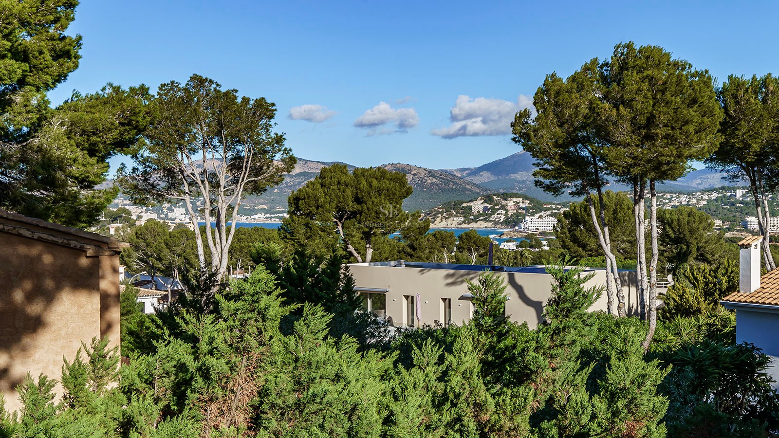 Villa moderna entre pinos con vistas al mar Mediterráneo y las montañas de fondo.
