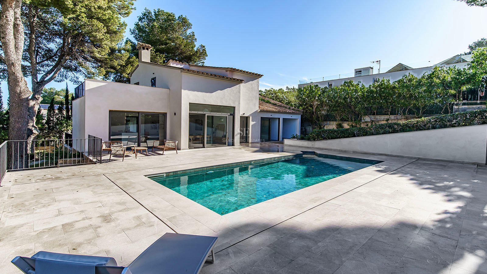 Villa blanca moderna con piscina rectangular turquesa y terraza de piedra rodeada de pinos.