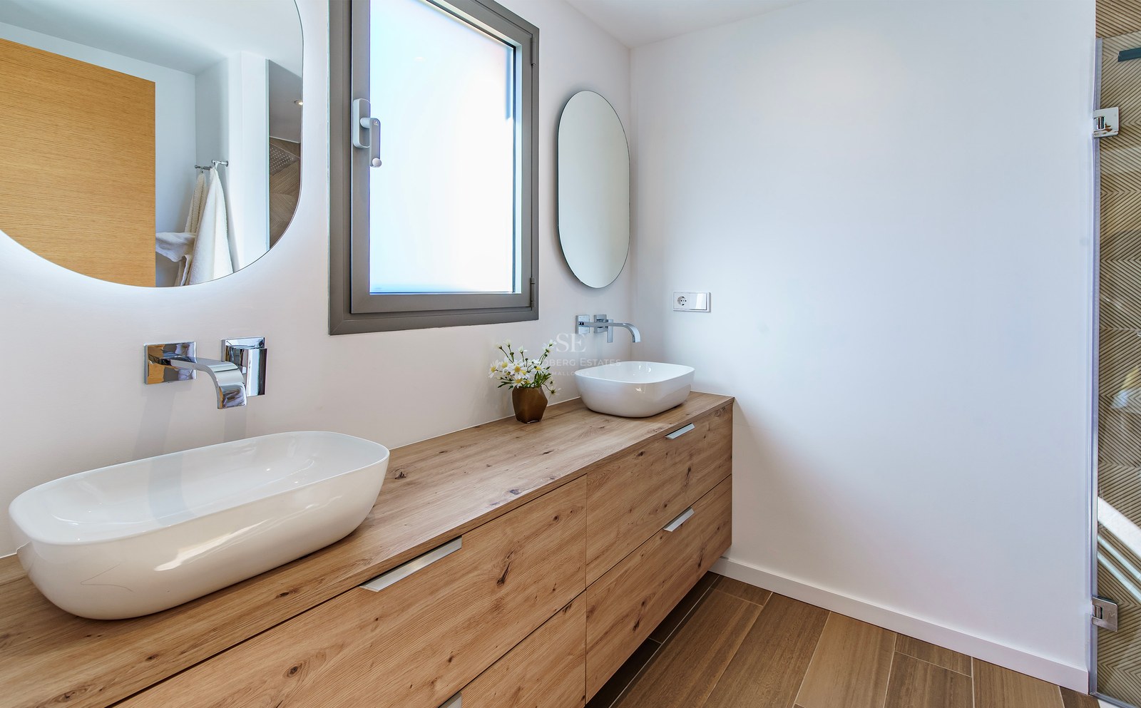 Salle de bain moderne avec un long meuble en bois, deux vasques blanches et des miroirs circulaires rétroéclairés.