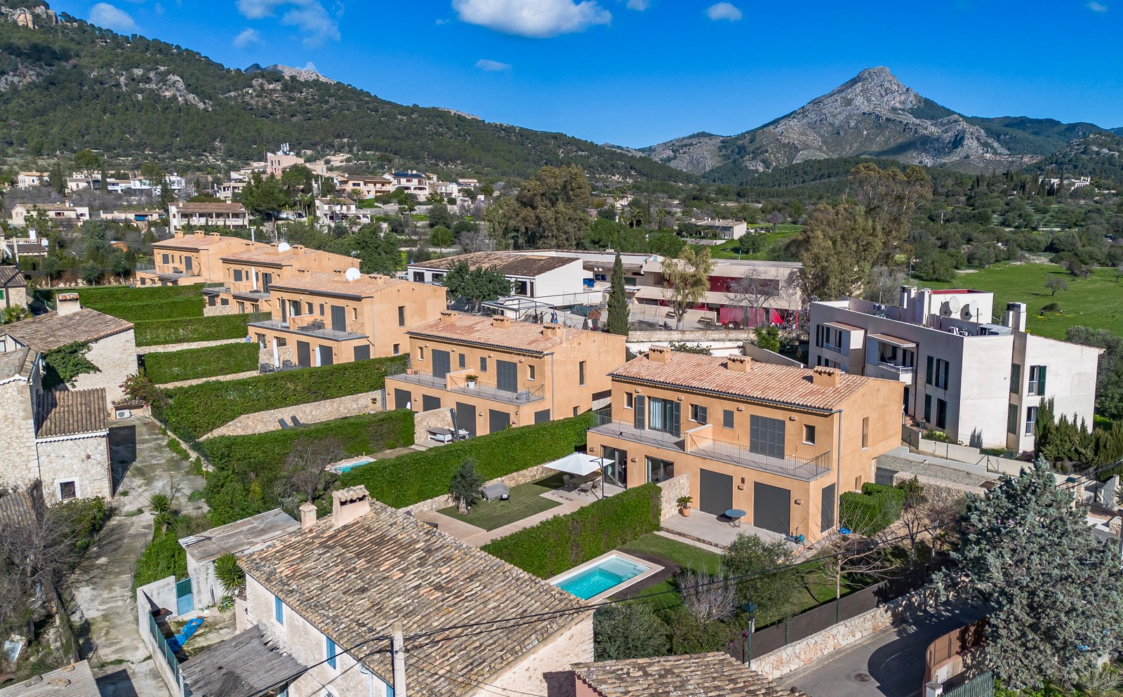 Vue aérienne de villas couleur terre cuite avec piscines privées et haies vertes sur fond de montagnes.