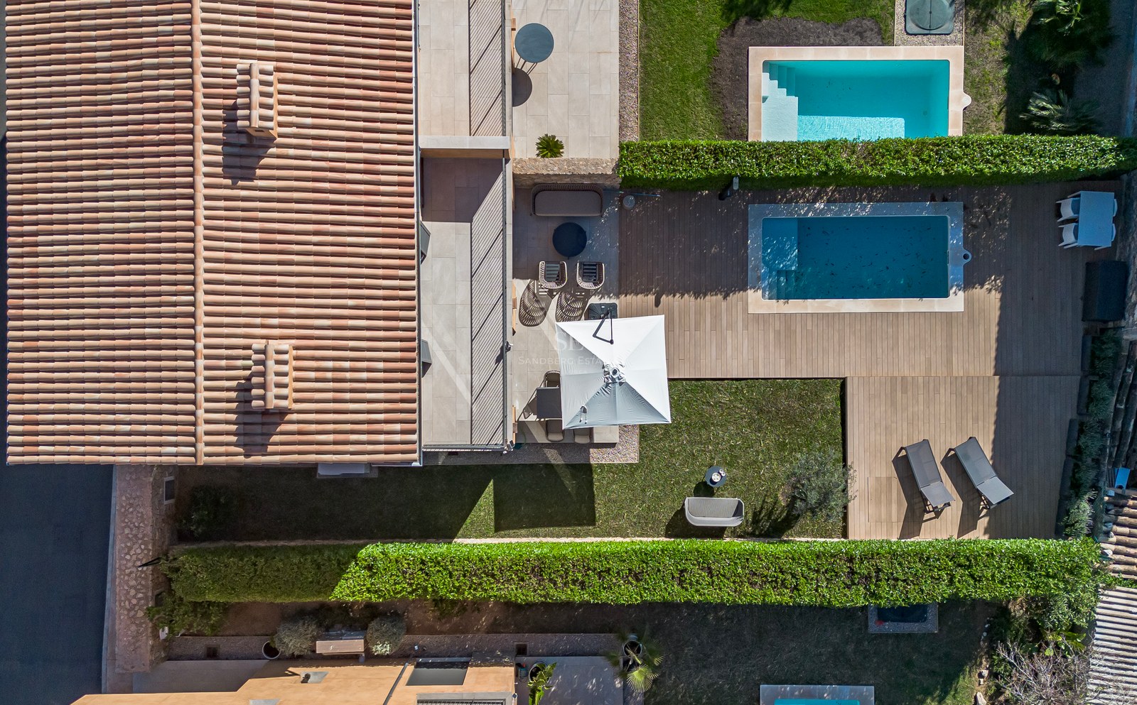 Vue d'oiseau d'une villa méditerranéenne avec toit en terre cuite, terrasse en bois, piscine et pelouse verdoyante.