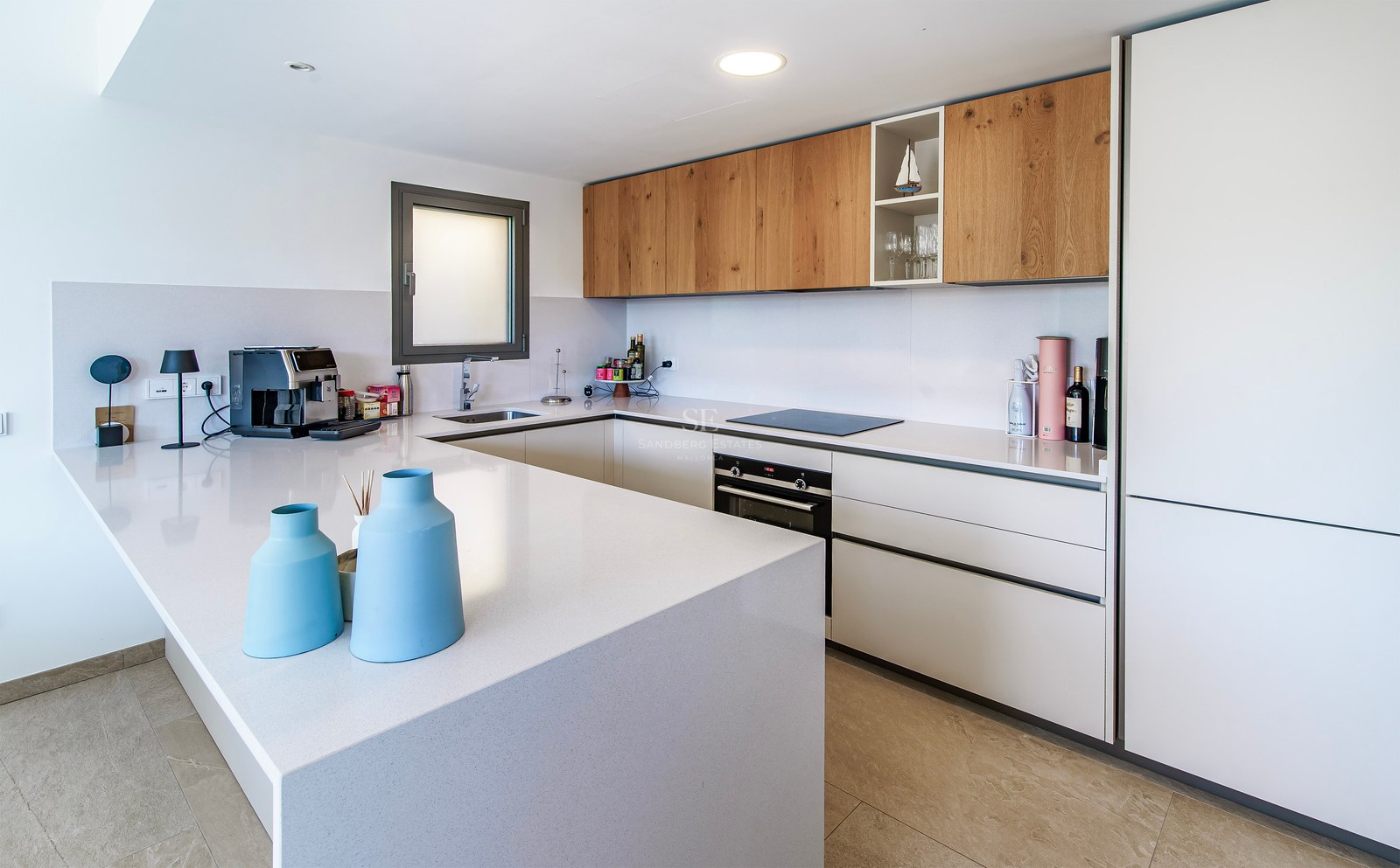 Cuisine blanche moderne avec meubles hauts en bois, grand îlot blanc et appareils encastrés.