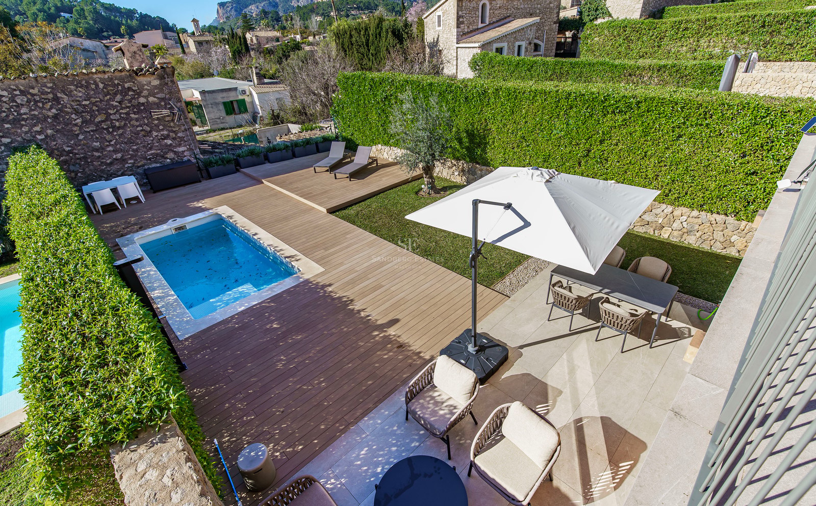 Vue de dessus d'une piscine rectangulaire, d'une terrasse en bois, d'une pelouse et d'un coin repas extérieur entourés de haies.