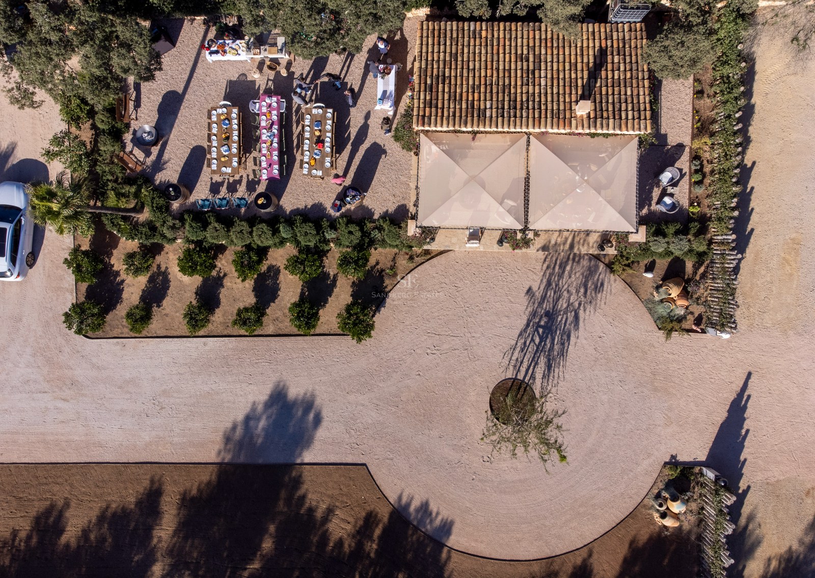 Vue plongeante d'une villa de luxe montrant les toits de tuiles, un espace repas extérieur et une allée circulaire.