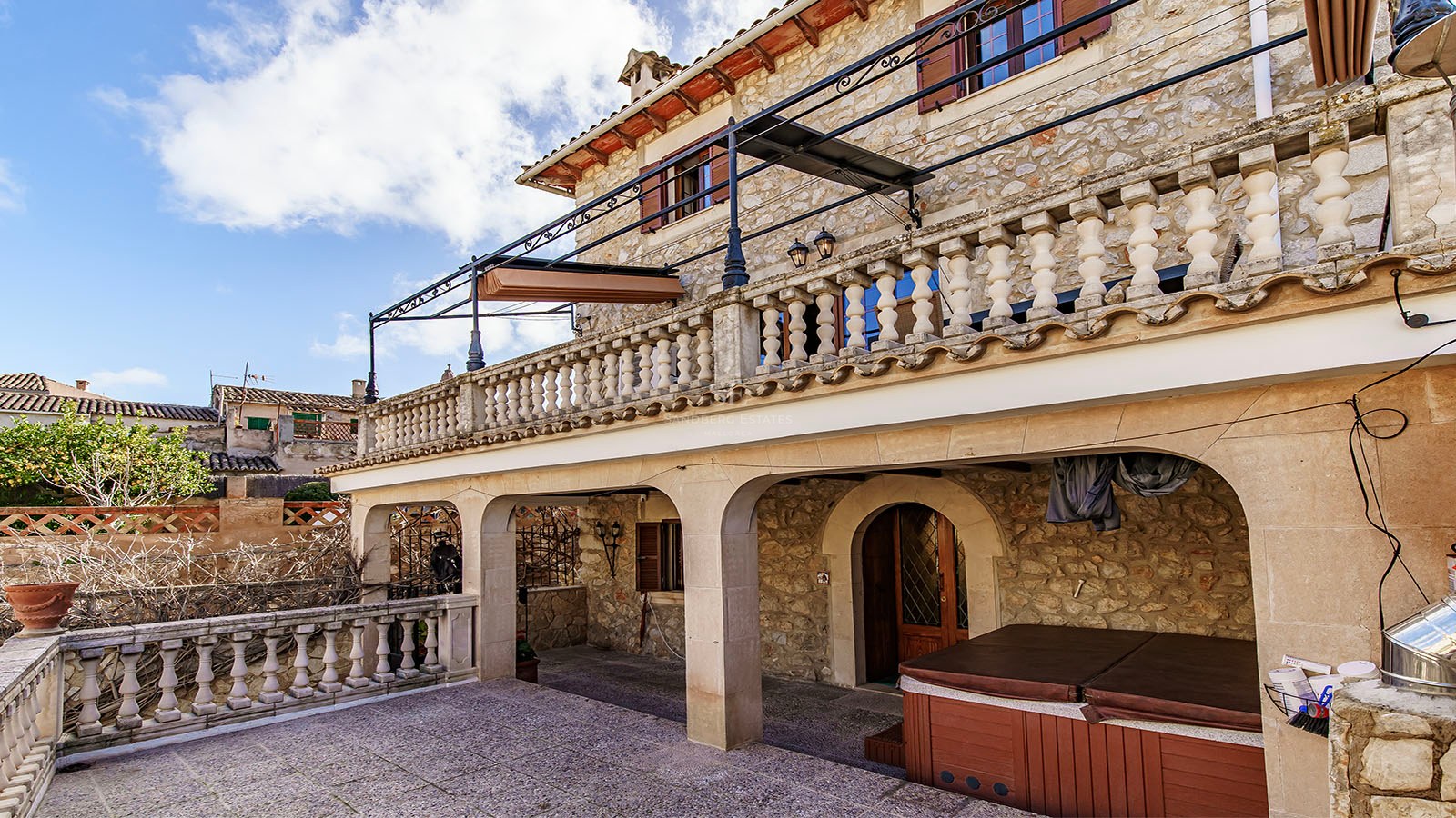 Tvåvånings stenfasad med valvportik, terrass med balustrad och övertäckt utomhusjacuzzi.