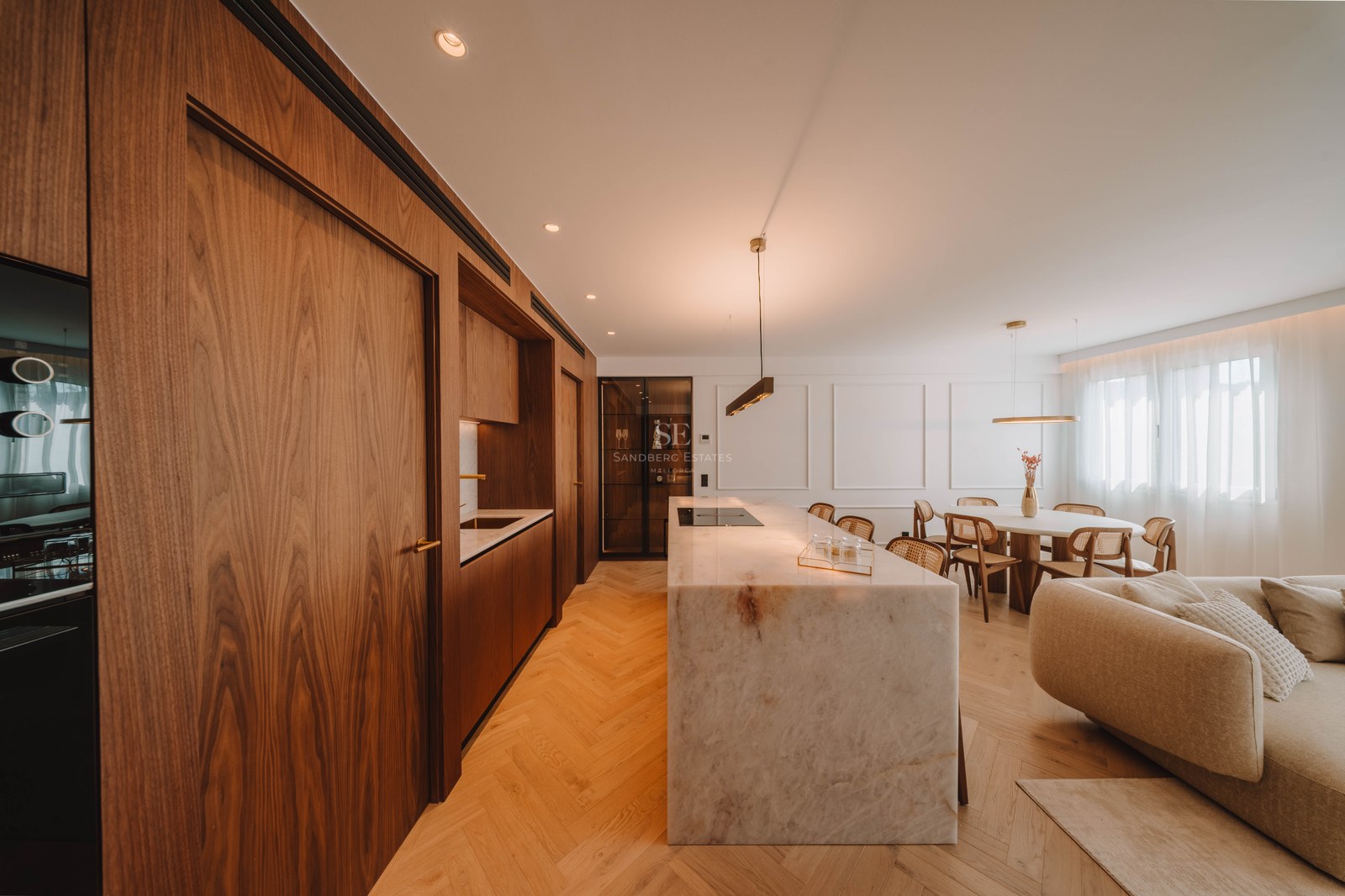 Modern open-plan kitchen featuring a large marble island, walnut cabinetry, and herringbone wood floors.