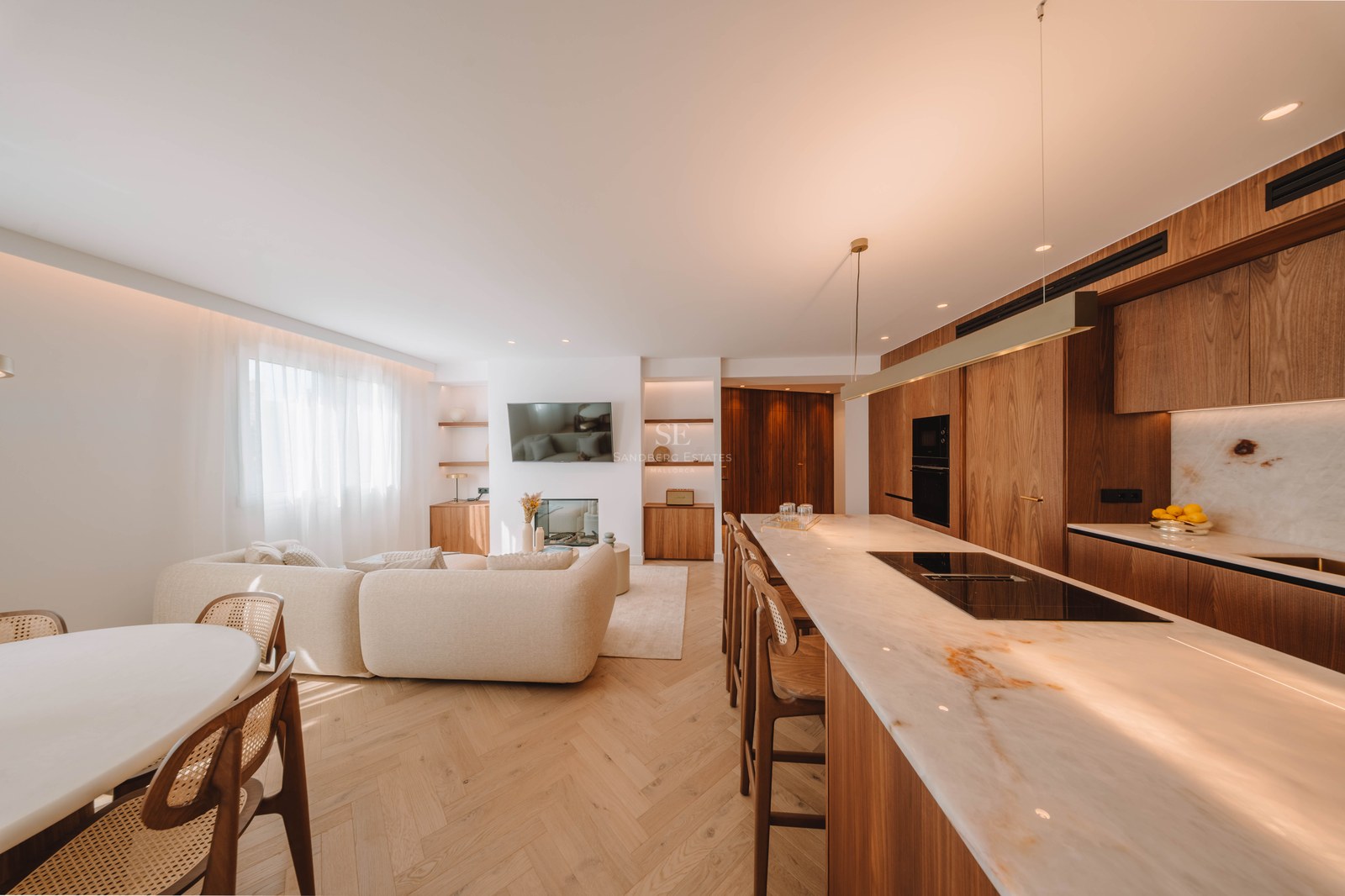 Bright open-concept living area with a beige sofa, marble kitchen island, and warm wood flooring.