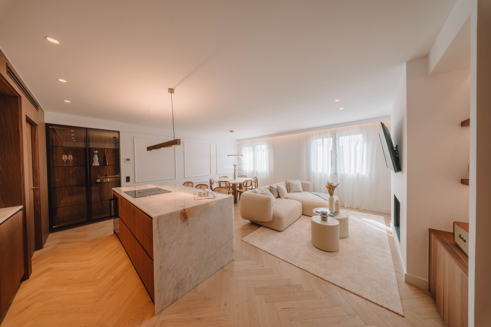 Bright open-plan living room with a large marble kitchen island, curved beige sofa, and herringbone wood floors.