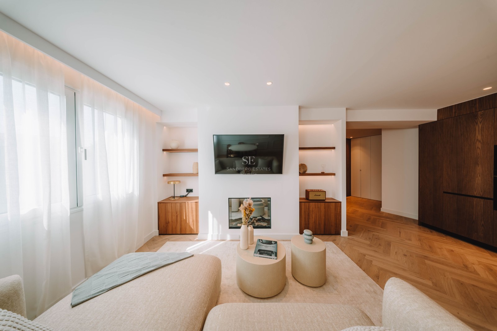 Bright living room featuring a wall-mounted TV, electric fireplace, herringbone wood floors, and cream sofas.