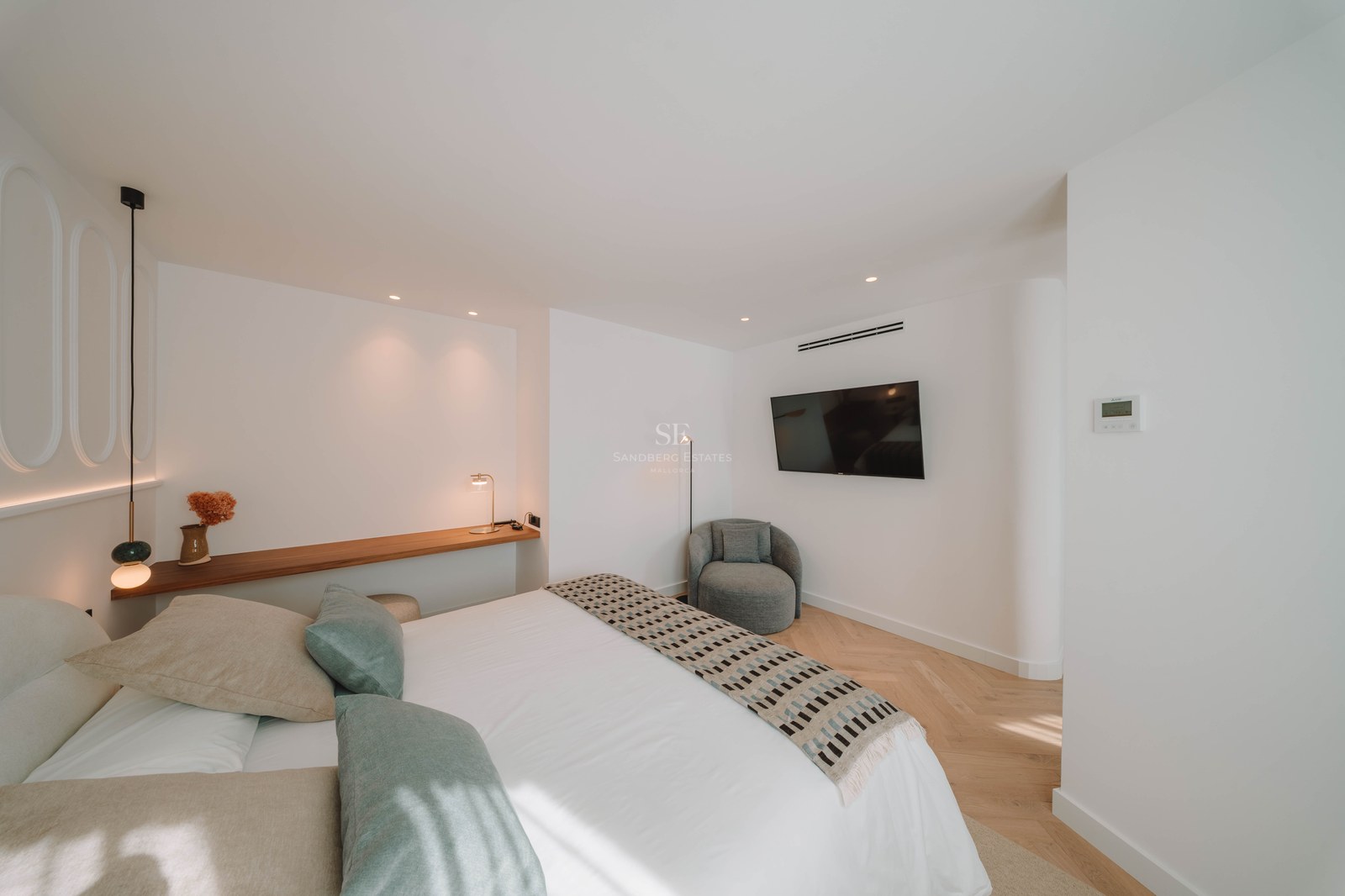Modern bedroom featuring a white bed with sage green pillows, wooden shelf, and herringbone wood flooring.