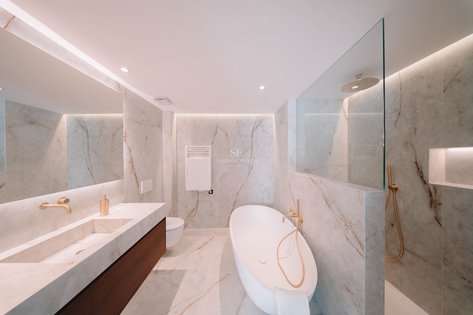 Modern marble bathroom featuring a white freestanding tub, gold fixtures, and an integrated double vanity.