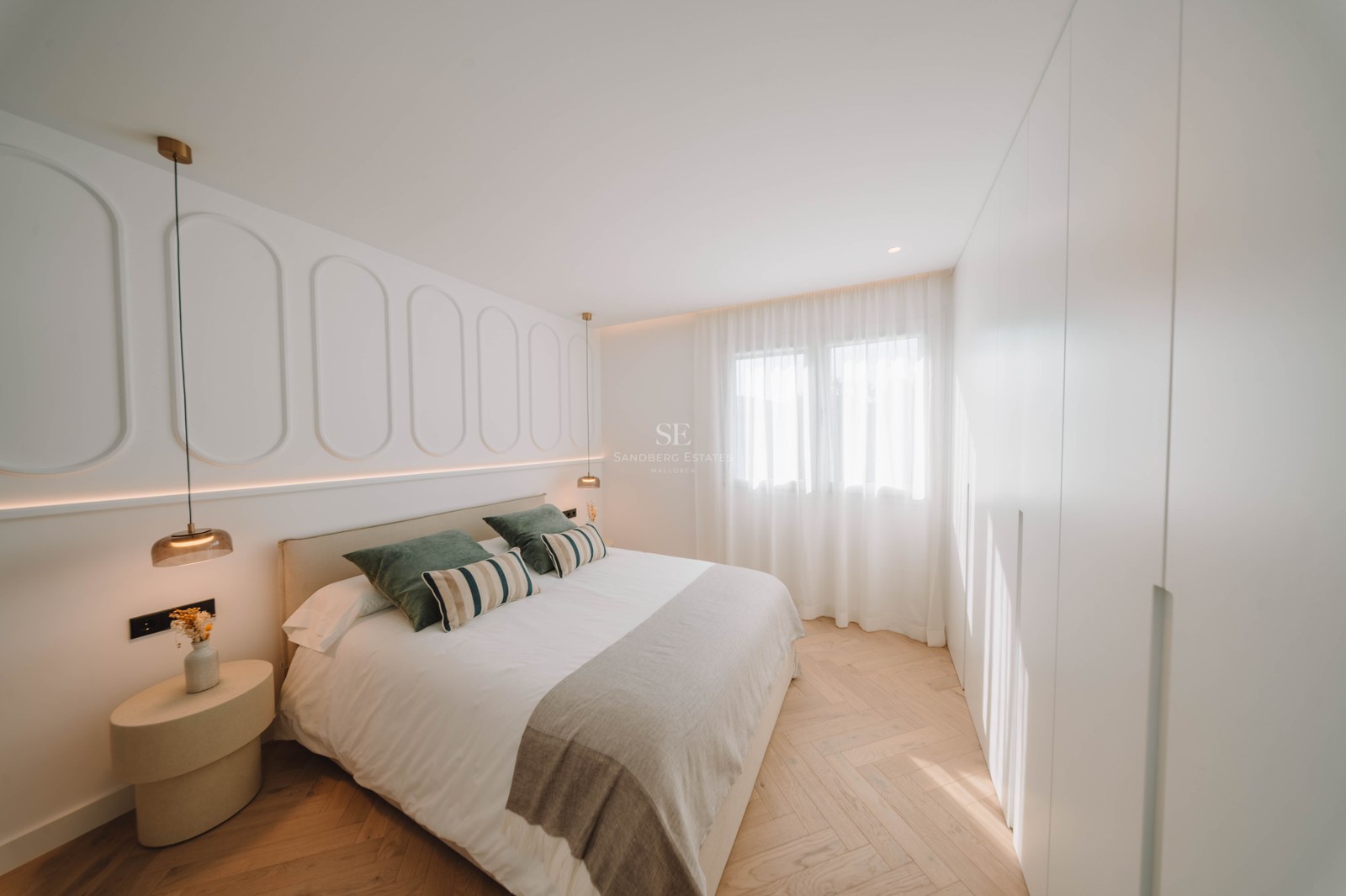 Modern master bedroom featuring a double bed, decorative wall molding, and light wood herringbone floors.