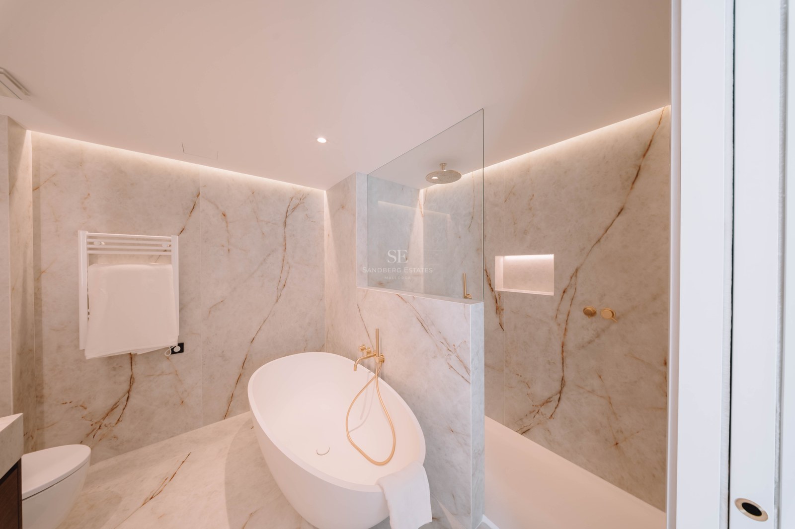 Elegant bathroom featuring a freestanding oval tub, glass shower, and marble walls with gold fixtures.