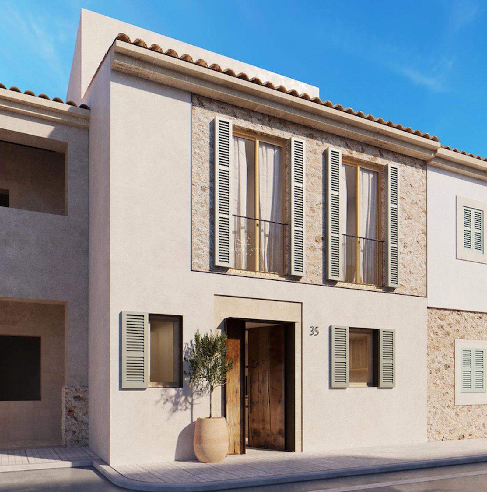 Beige stucco building with sage green shutters, natural stone accents, and a wooden door under a clear blue sky.