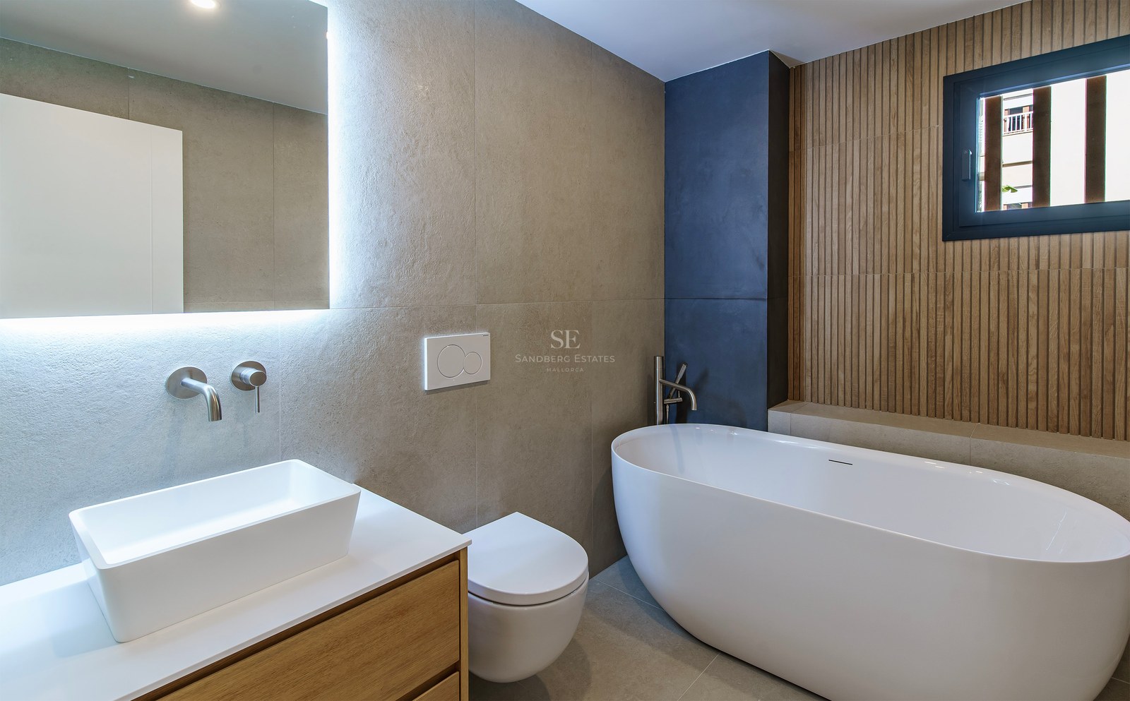 Modern bathroom featuring a freestanding oval tub, a white vessel sink on wood vanity, and a backlit mirror.