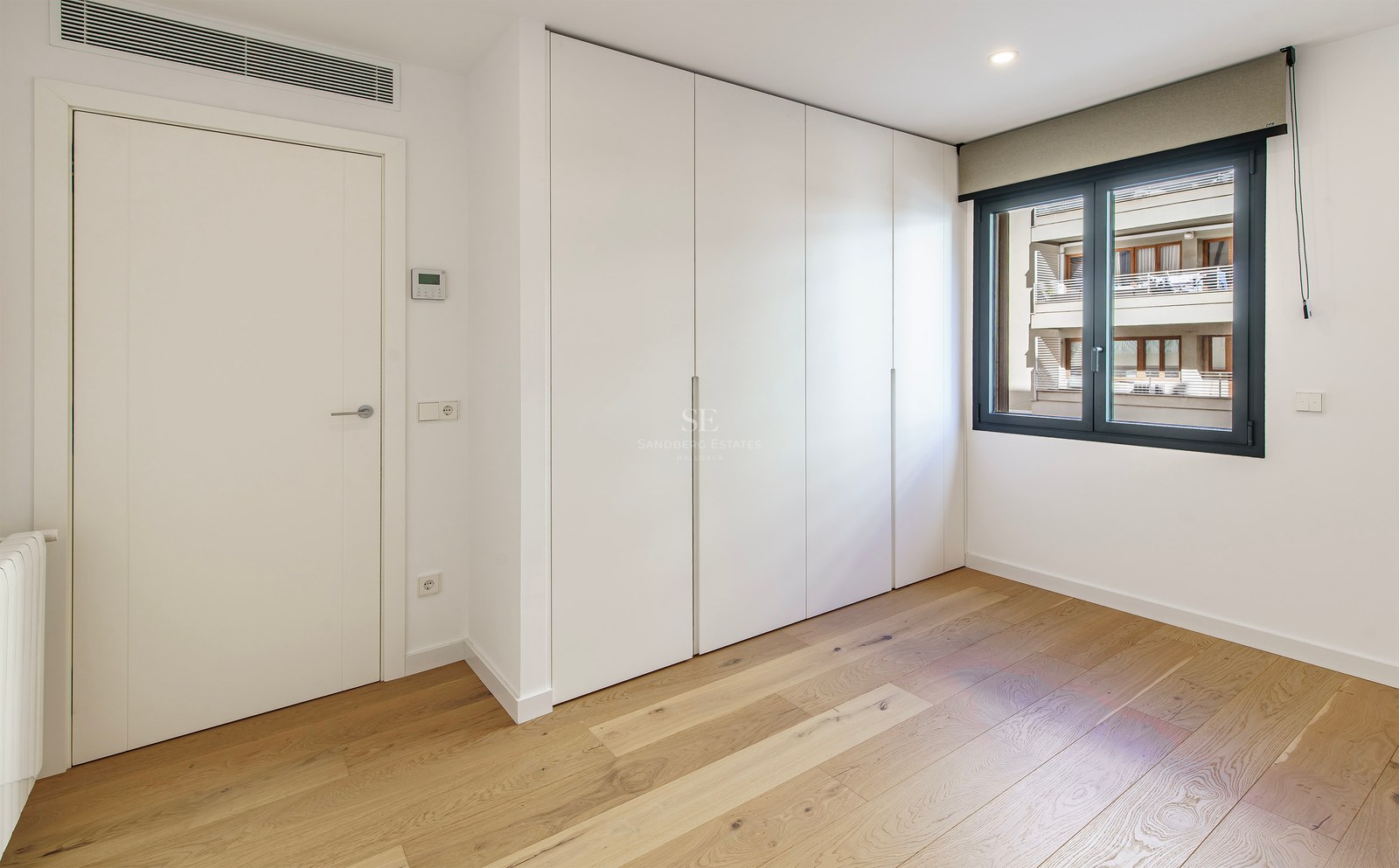 Bright room with light wood floors, large white built-in closets, a white door, and a window with a dark frame.