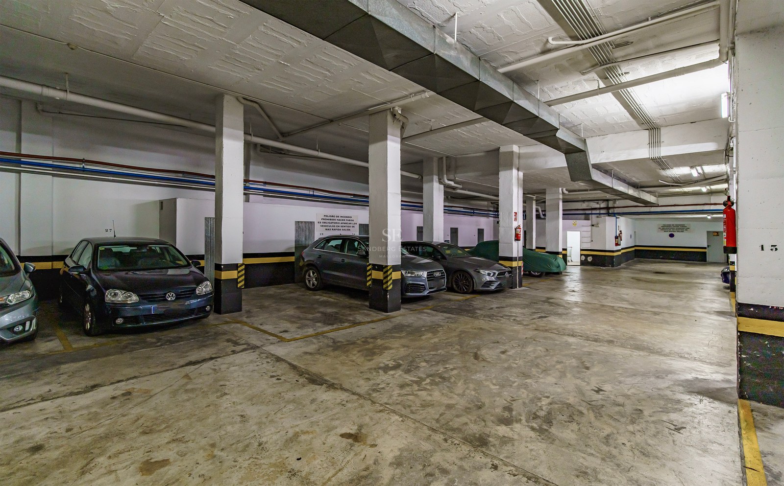 Spacious underground garage with concrete pillars, yellow safety markings, and parked cars.