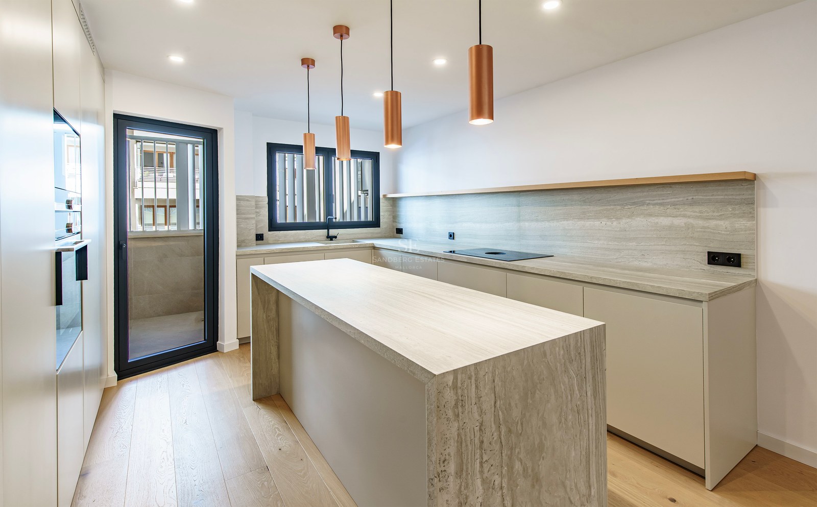 Bright kitchen featuring a large travertine stone island, copper pendant lights, and light wood flooring.