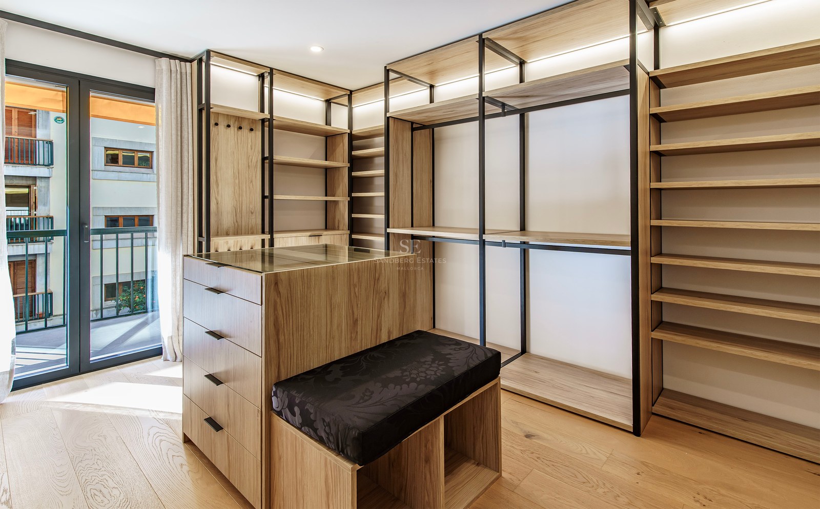 Modern walk-in closet with light wood shelving, black metal frames, a central island, and balcony access.