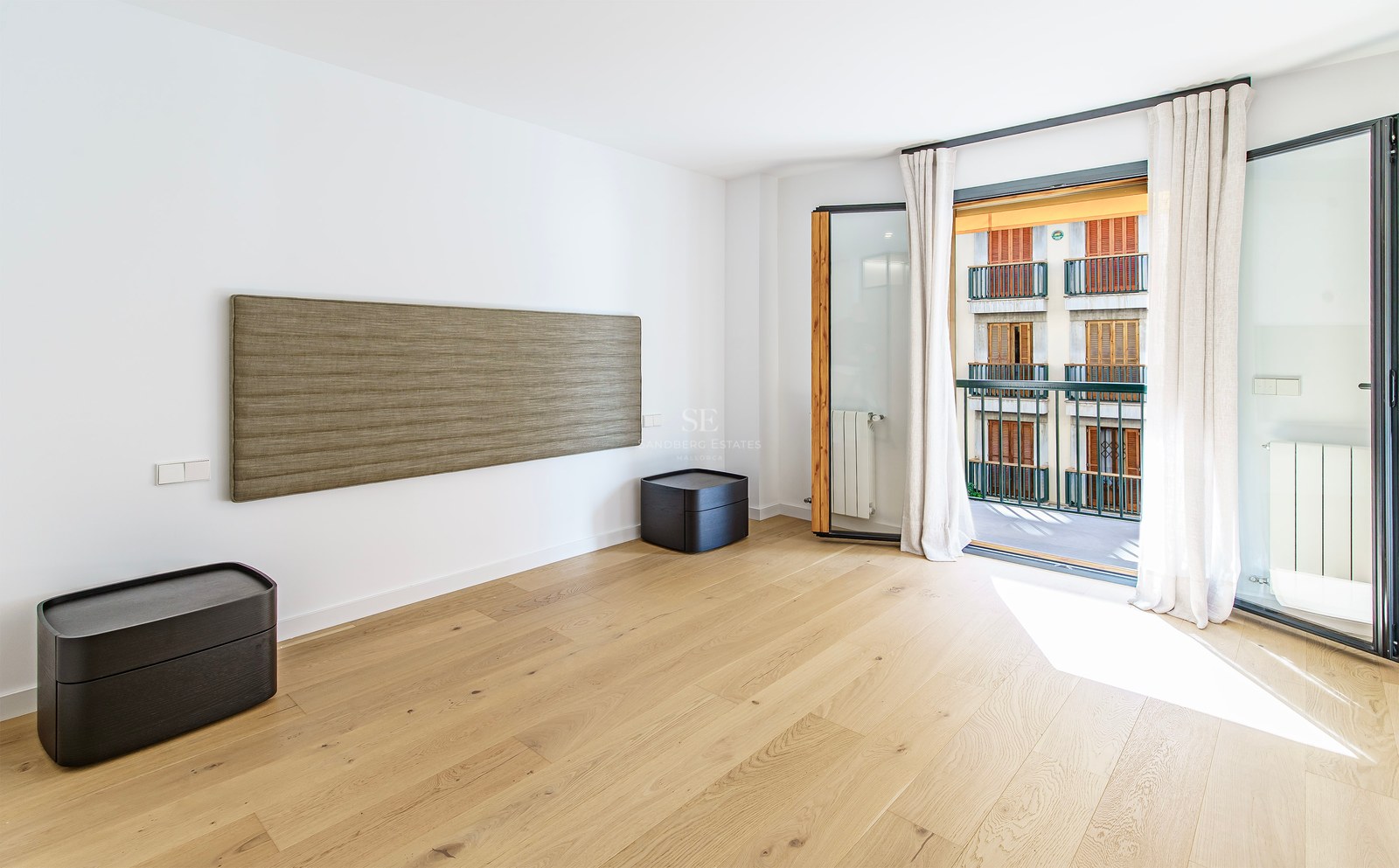 Modern bedroom with light wood floors, a textured wall-mounted headboard, and balcony doors with natural light.