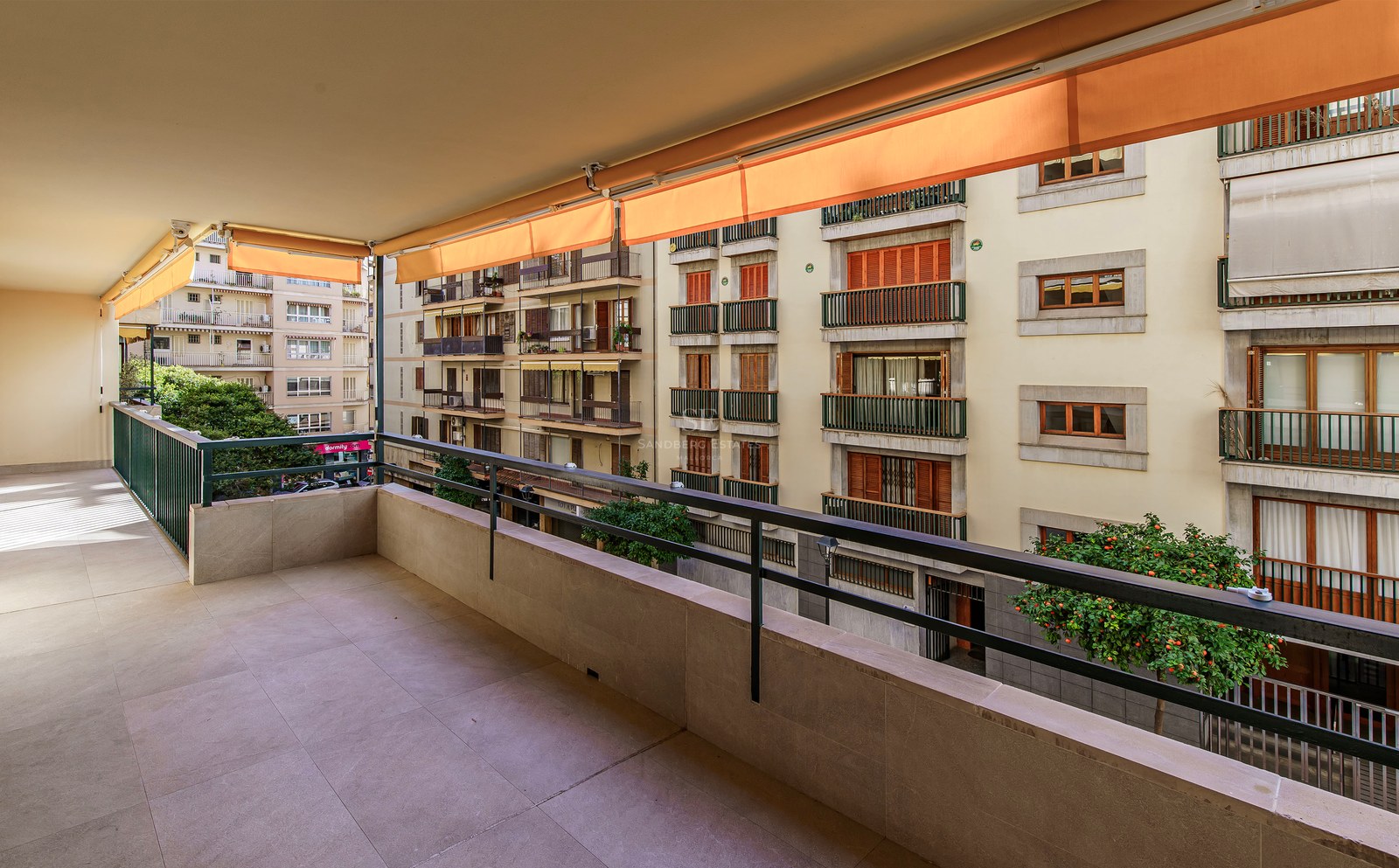 Wide stone terrace with metal railing and orange retractable awnings overlooking residential buildings.