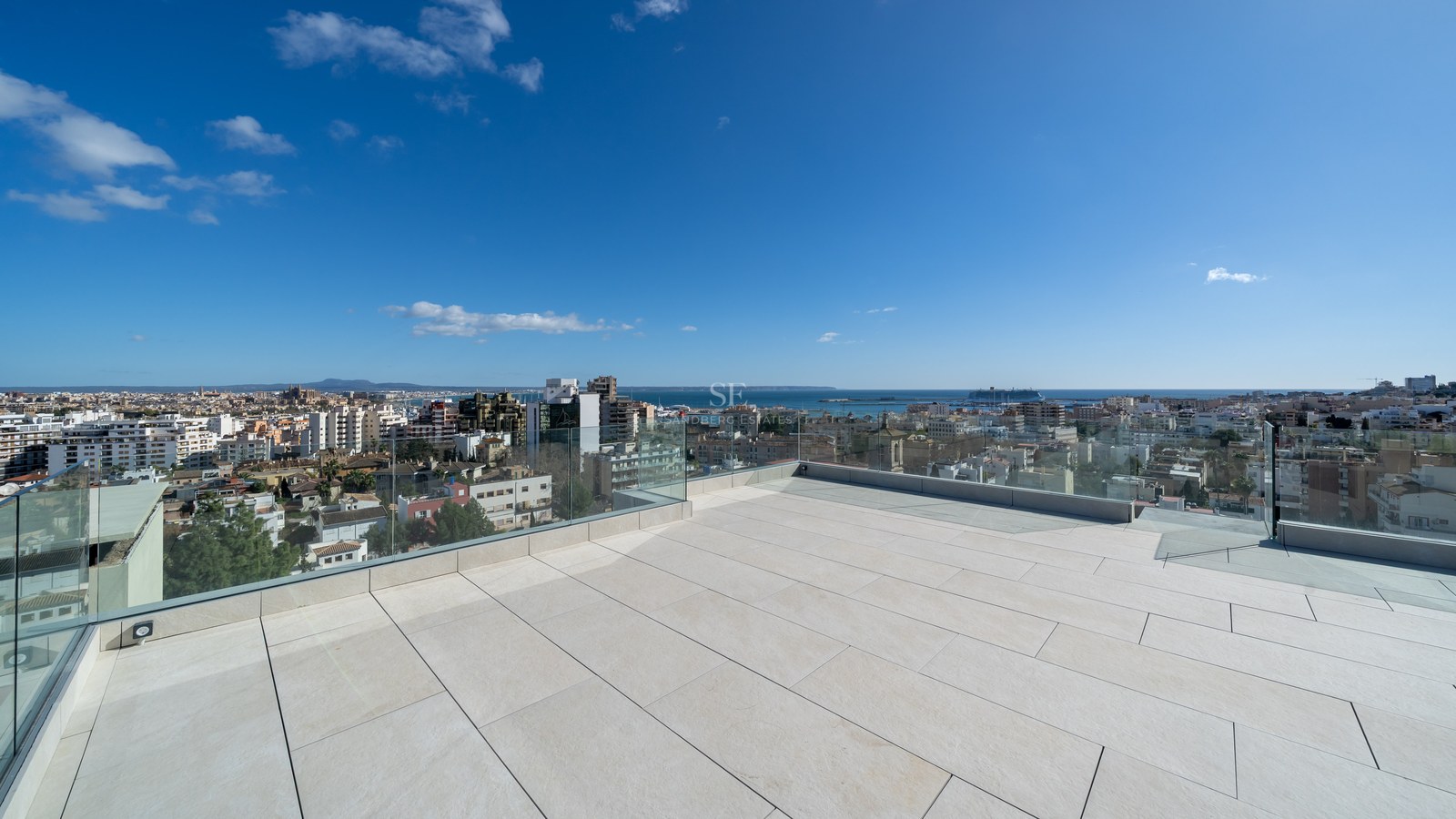 Stor takterrass med ljusa stenplattor och glasräcken med utsikt över Palma stad, katedralen och havet.