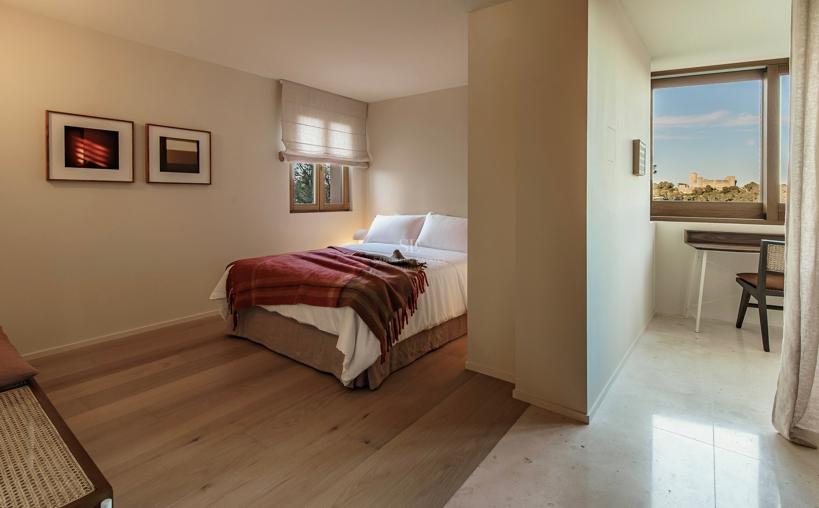Minimalistisches Schlafzimmer mit weißem Bett, Holzböden und Arbeitsbereich mit Blick auf eine historische Burg.