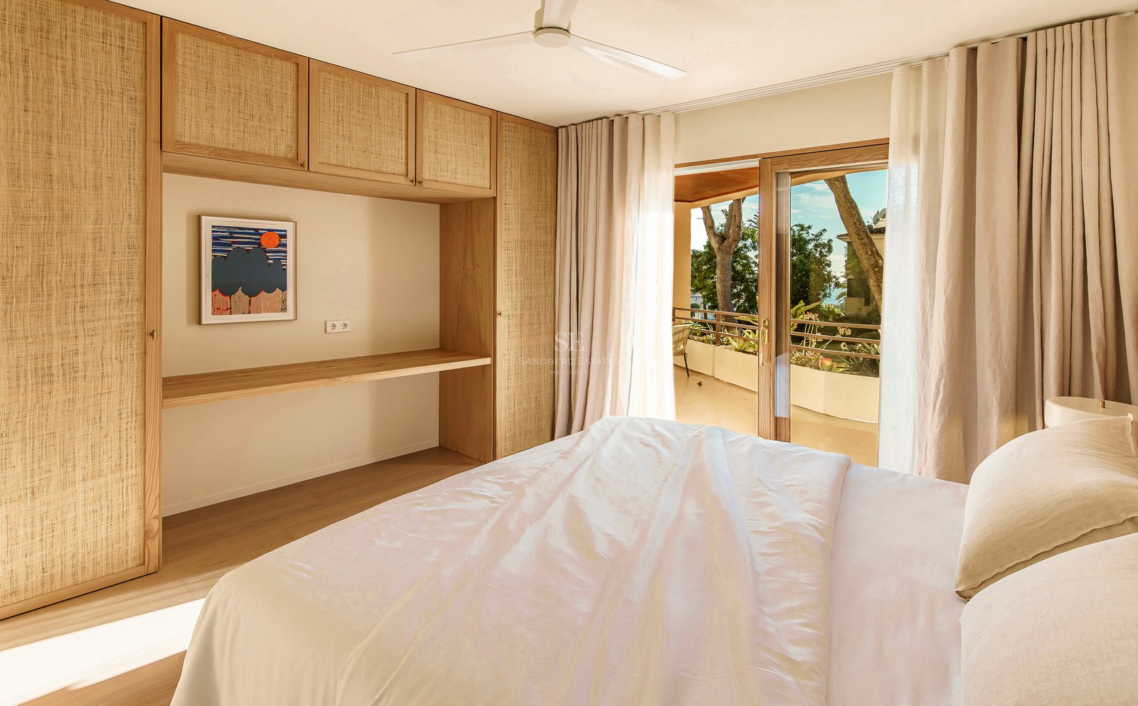 Helles Schlafzimmer mit Einbauschränken aus hellem Holz, Schreibtisch und Schiebetüren zu einer sonnigen Terrasse.