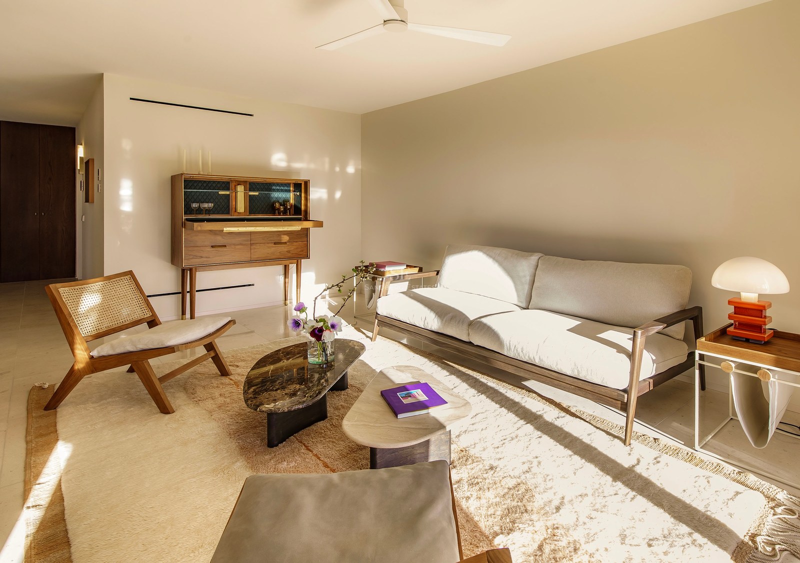 Helles Wohnzimmer mit Mid-Century-Möbeln, Marmortisch, Holzschrank und sonnendurchflutetem cremefarbenem Sofa.