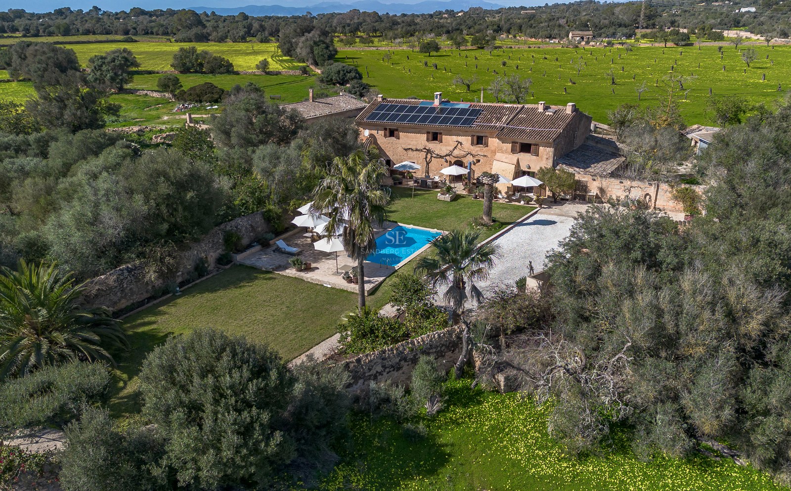Luftaufnahme einer traditionellen Steinfinca mit Swimmingpool, Sonnenkollektoren und weitläufigen Gärten auf Mallorca.