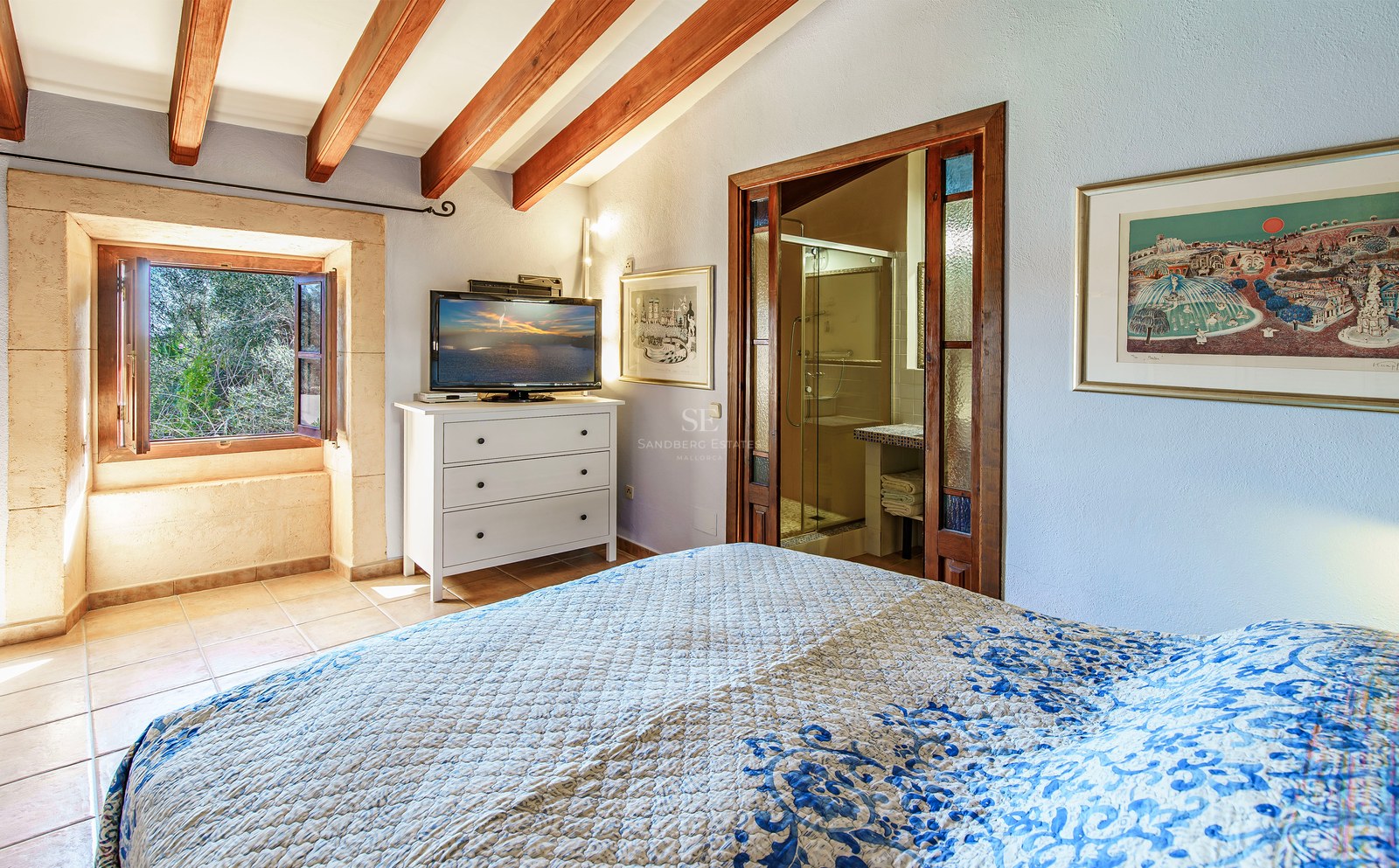 Schlafzimmer mit Holzbalken, blau gemustertem Bett, sichtbarem Bad und Steinfenster mit Ausblick.