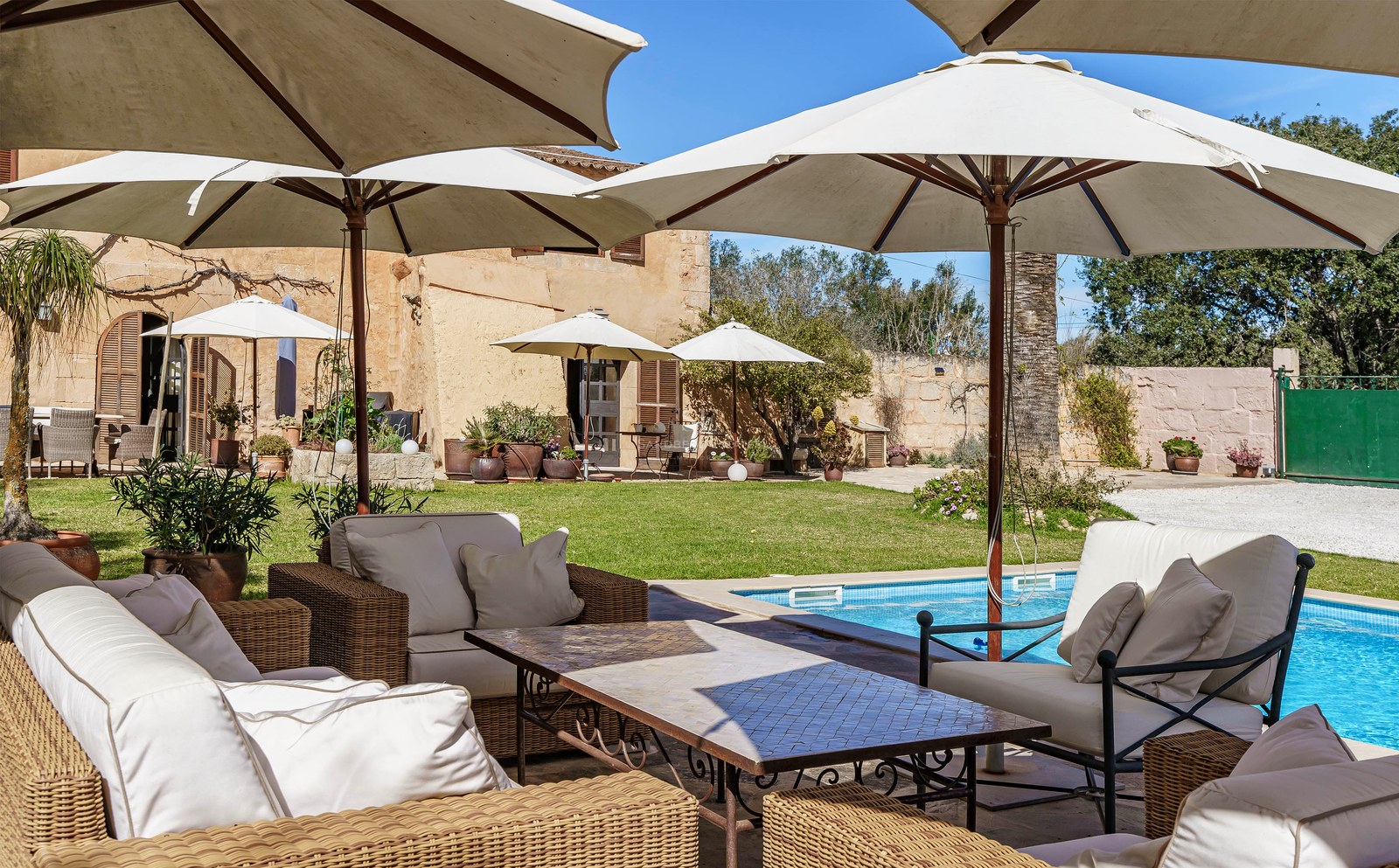Schwimmbad umgeben von großen weißen Sonnenschirmen und Loungemöbeln aus Korbgeflecht in einem mediterranen Garten.