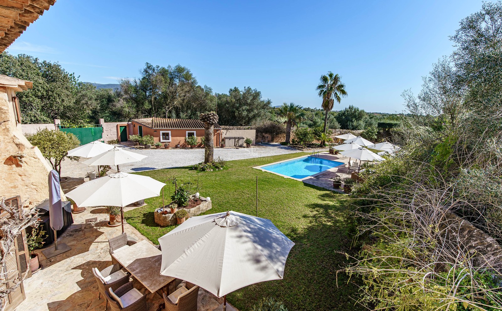 Rechteckiger Pool umgeben von grünem Rasen, Sonnenschirmen und einer Steinterrasse in einem mediterranen Anwesen.