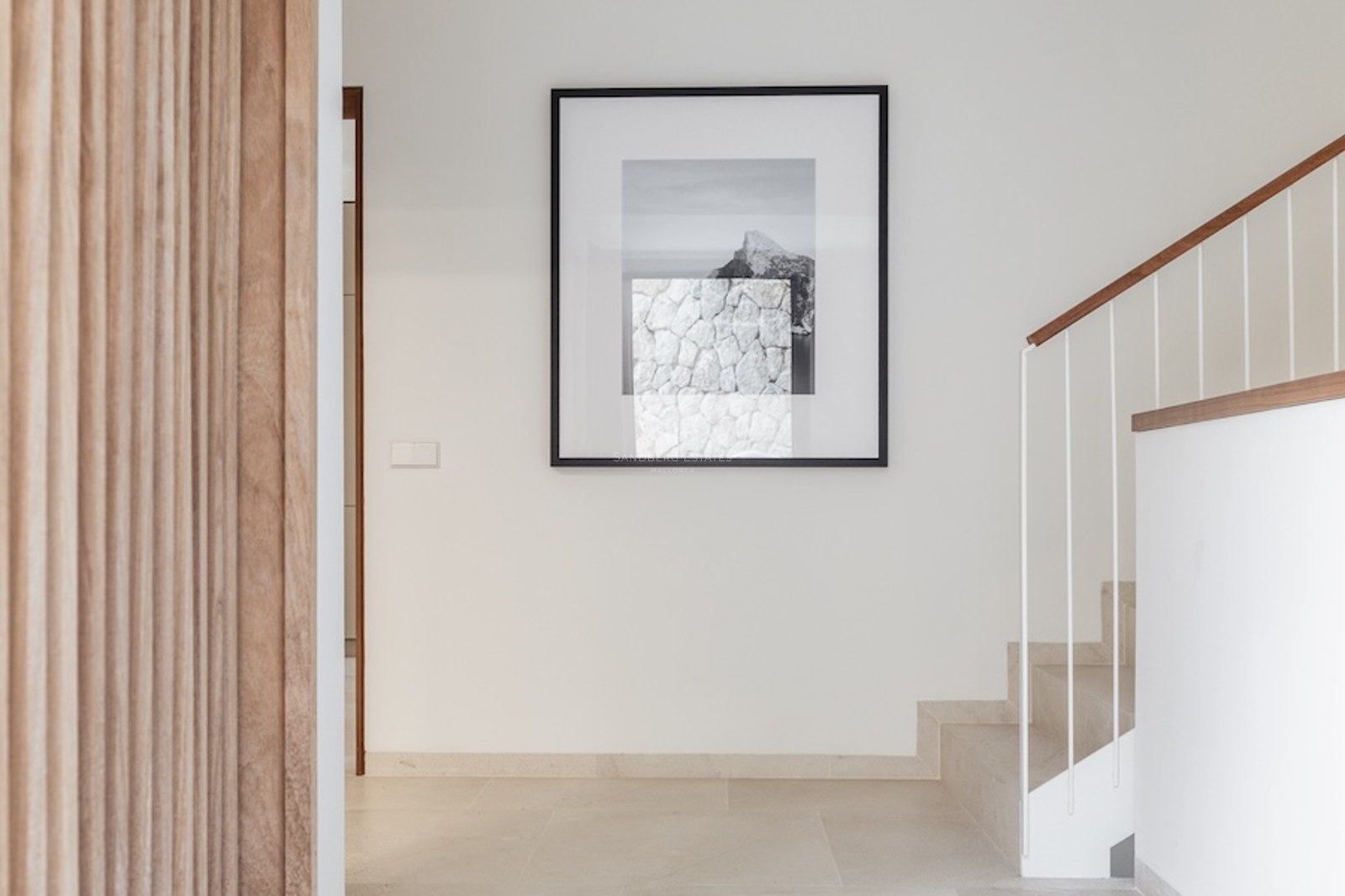 Minimalist hallway with stone stairs, a wooden handrail, and a large framed artwork on a white wall.