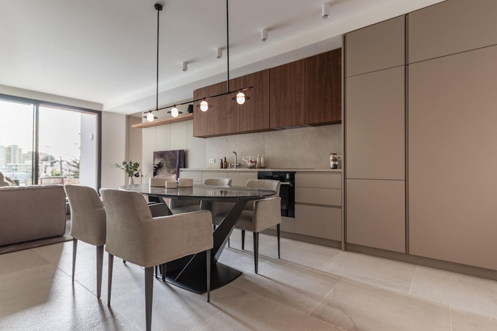Modern dining area with an oval dark marble table, beige chairs, and a minimalist kitchen with wood accents.