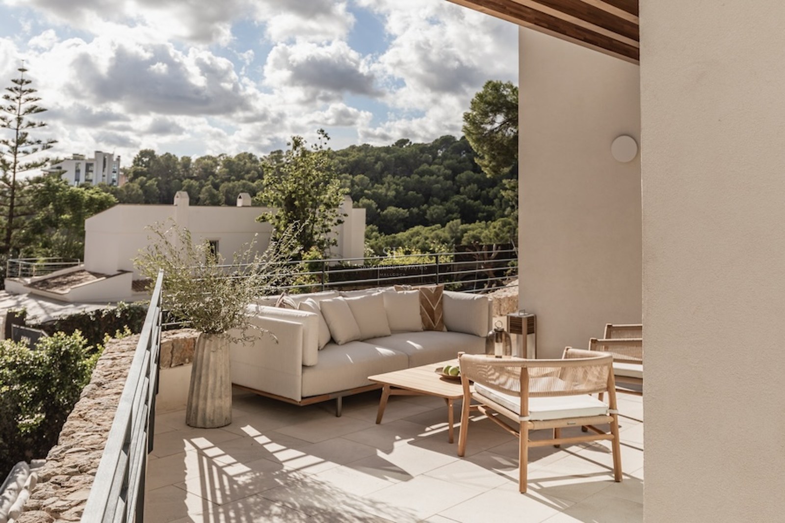 Outdoor terrace with modern sofa, wooden table, and woven chairs overlooking a lush green valley.