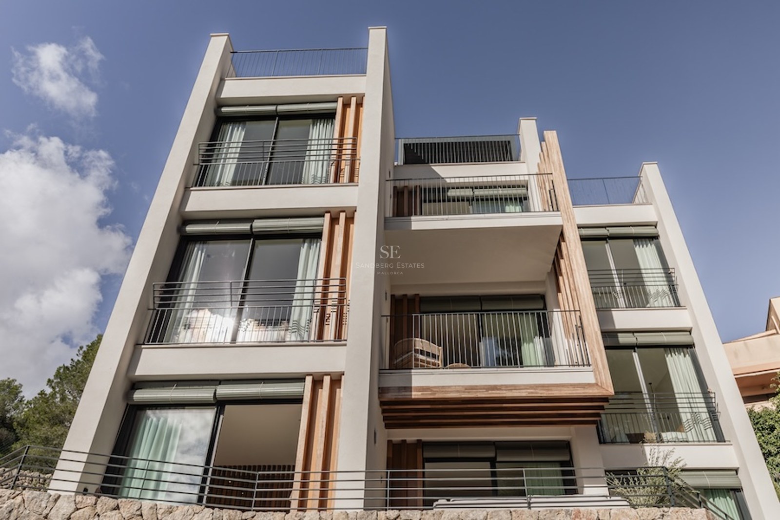 Low angle exterior view of a multi-story modern building with balconies, wood panels, and stone walls.