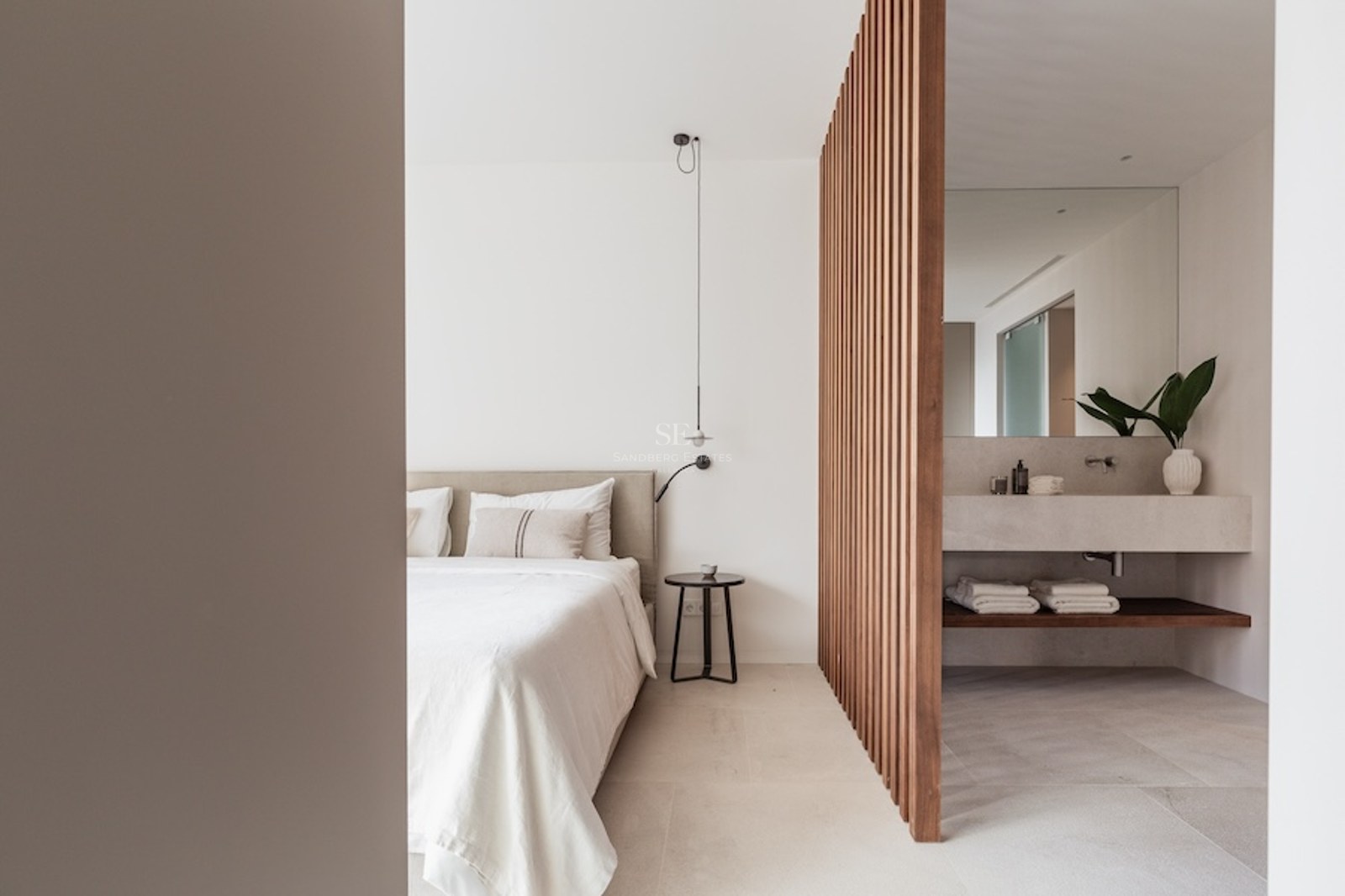 Modern bedroom with a beige bed and a wooden slat divider separating a stone vanity bathroom area.