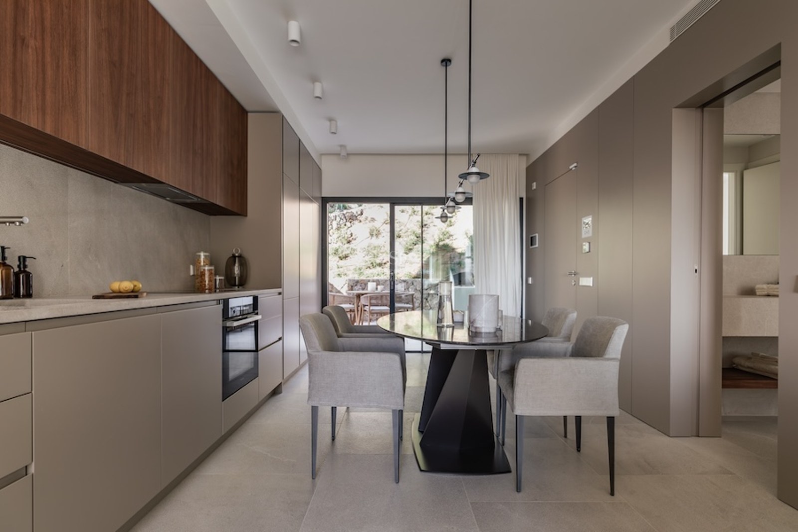 Minimalist kitchen with taupe and wood cabinetry, a grey dining table, and large glass doors leading to a terrace.