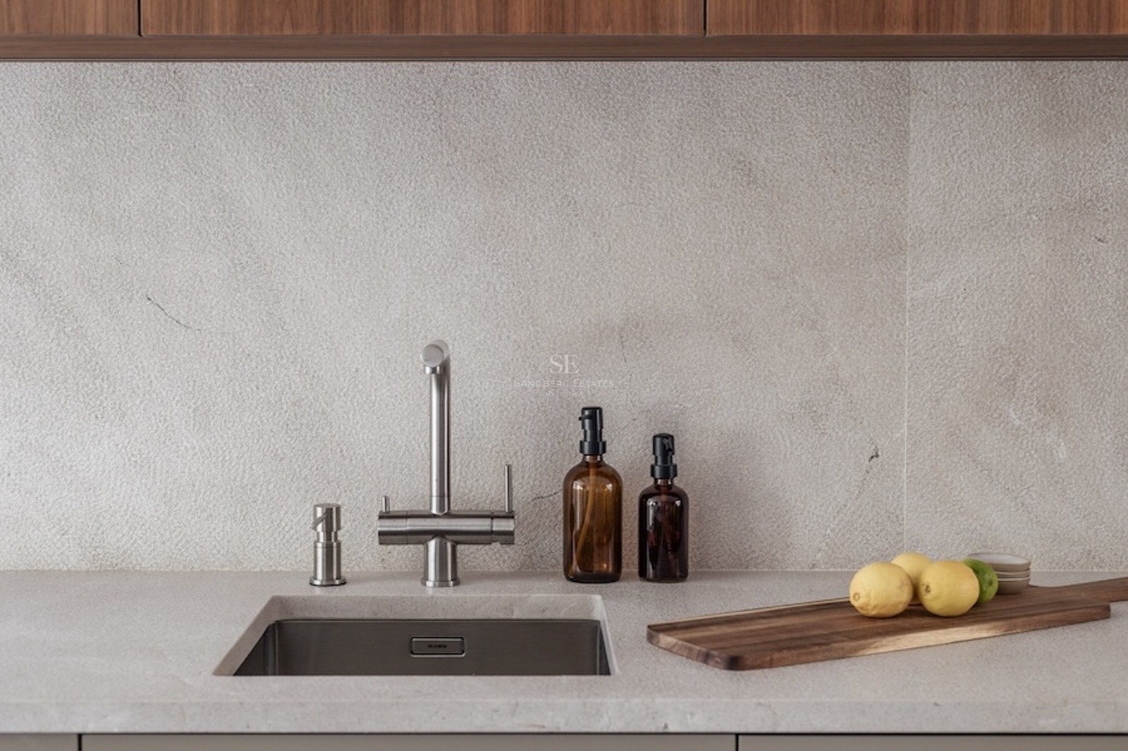 Close-up of a kitchen sink with a stainless steel faucet, stone countertop, and wooden cutting board.