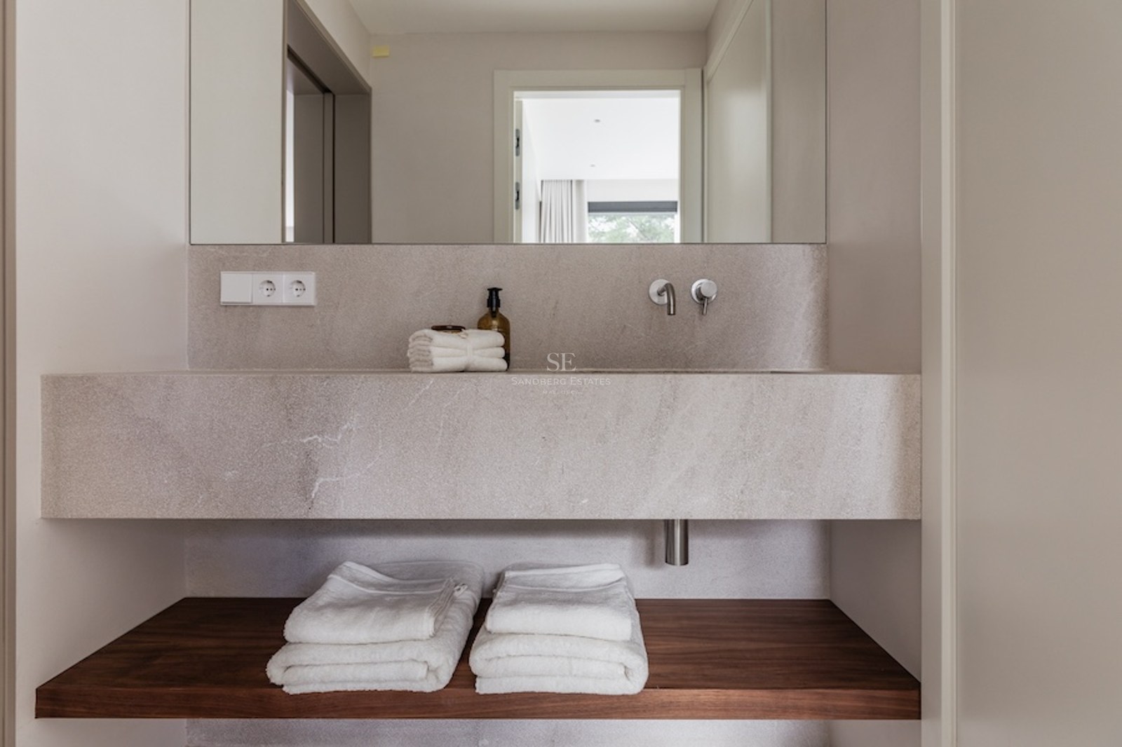 Close-up of a floating stone bathroom sink with a wooden shelf below and folded white towels.