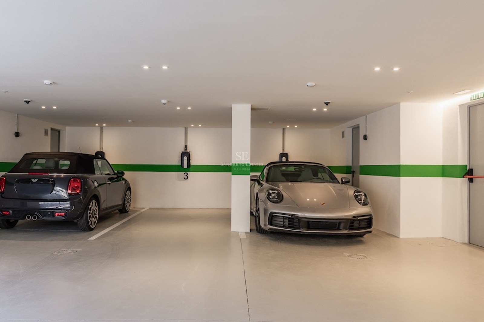 Interior of a modern underground garage with a silver Porsche and a black Mini, featuring EV wall chargers.