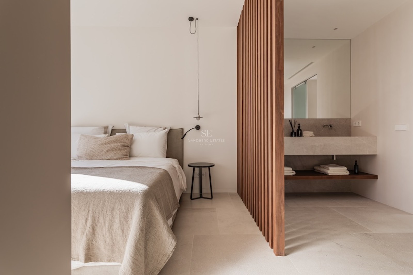 Minimalist beige bedroom separated from a stone vanity by vertical wooden slats.