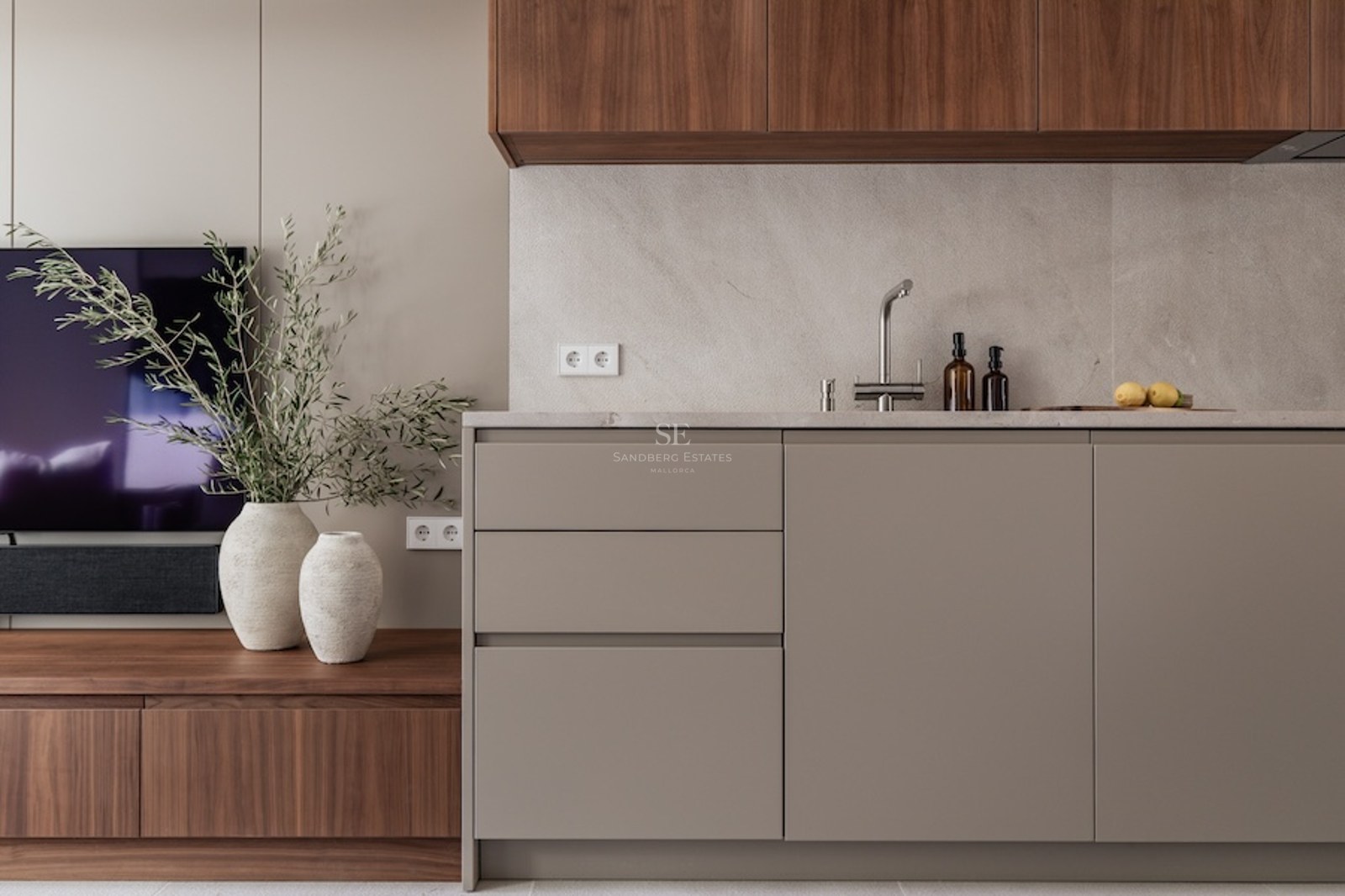 Modern kitchen with taupe cabinets, stone countertop, and walnut wood accents next to a TV unit.