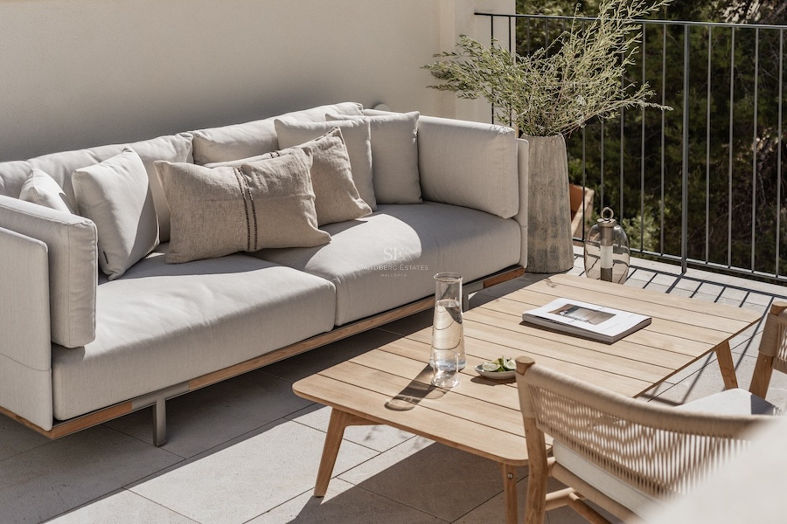 Moderne Terrasse mit einem grauen Sofa, Holztisch und dekorativen Pflanzen in mediterranem Ambiente.