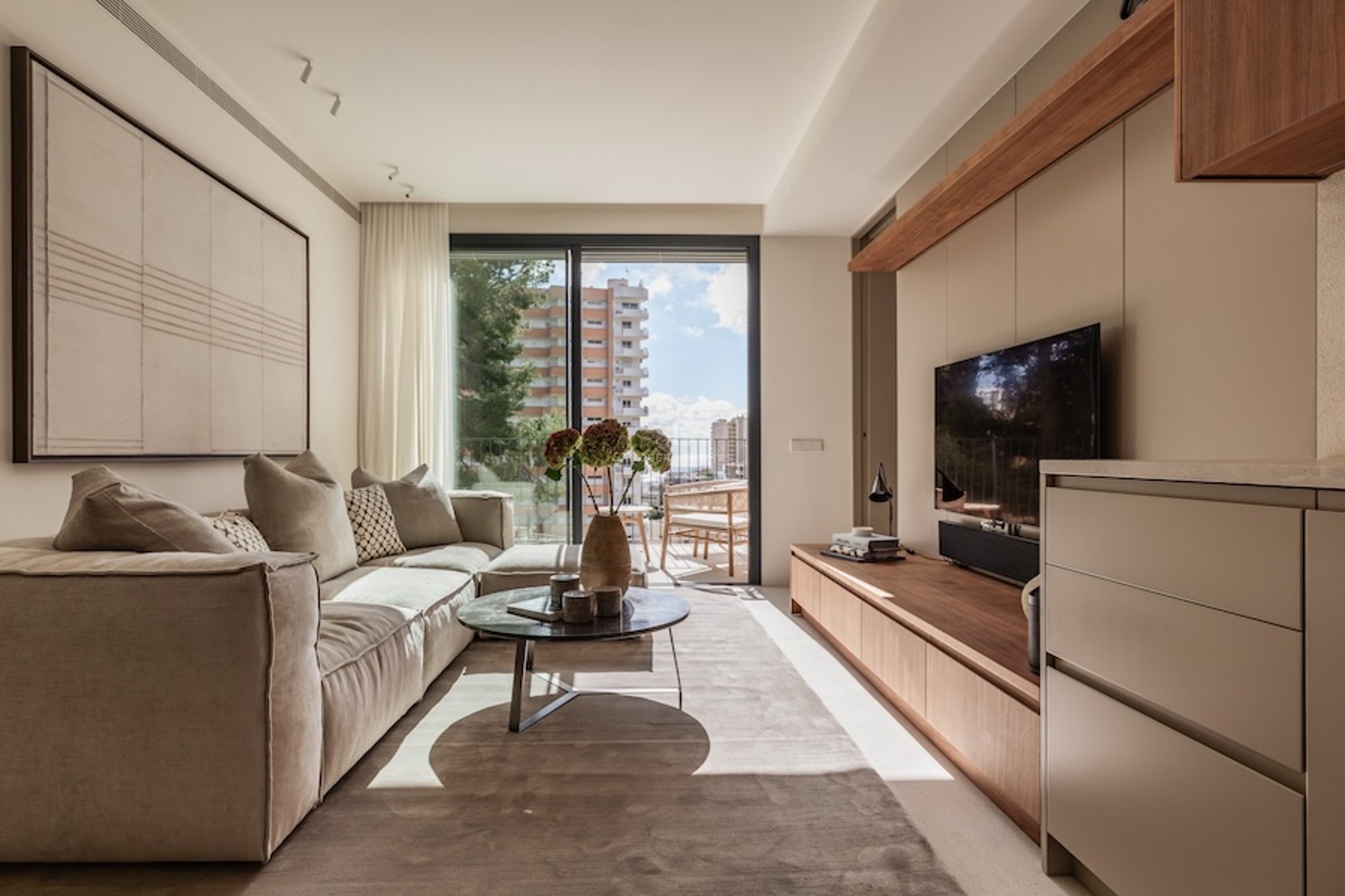 Helles Wohnzimmer mit großem beigem Sofa, Marmor-Couchtisch und Glasschiebetüren zum Balkon.