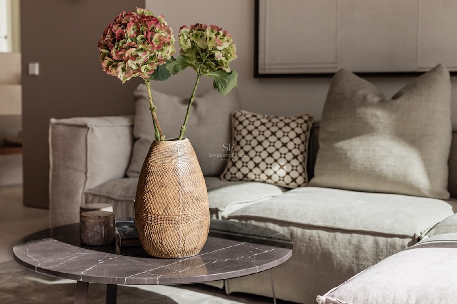 Nahaufnahme eines Couchtischs aus Marmor mit einer Vase Hortensien vor einem beigen Leinensofa.