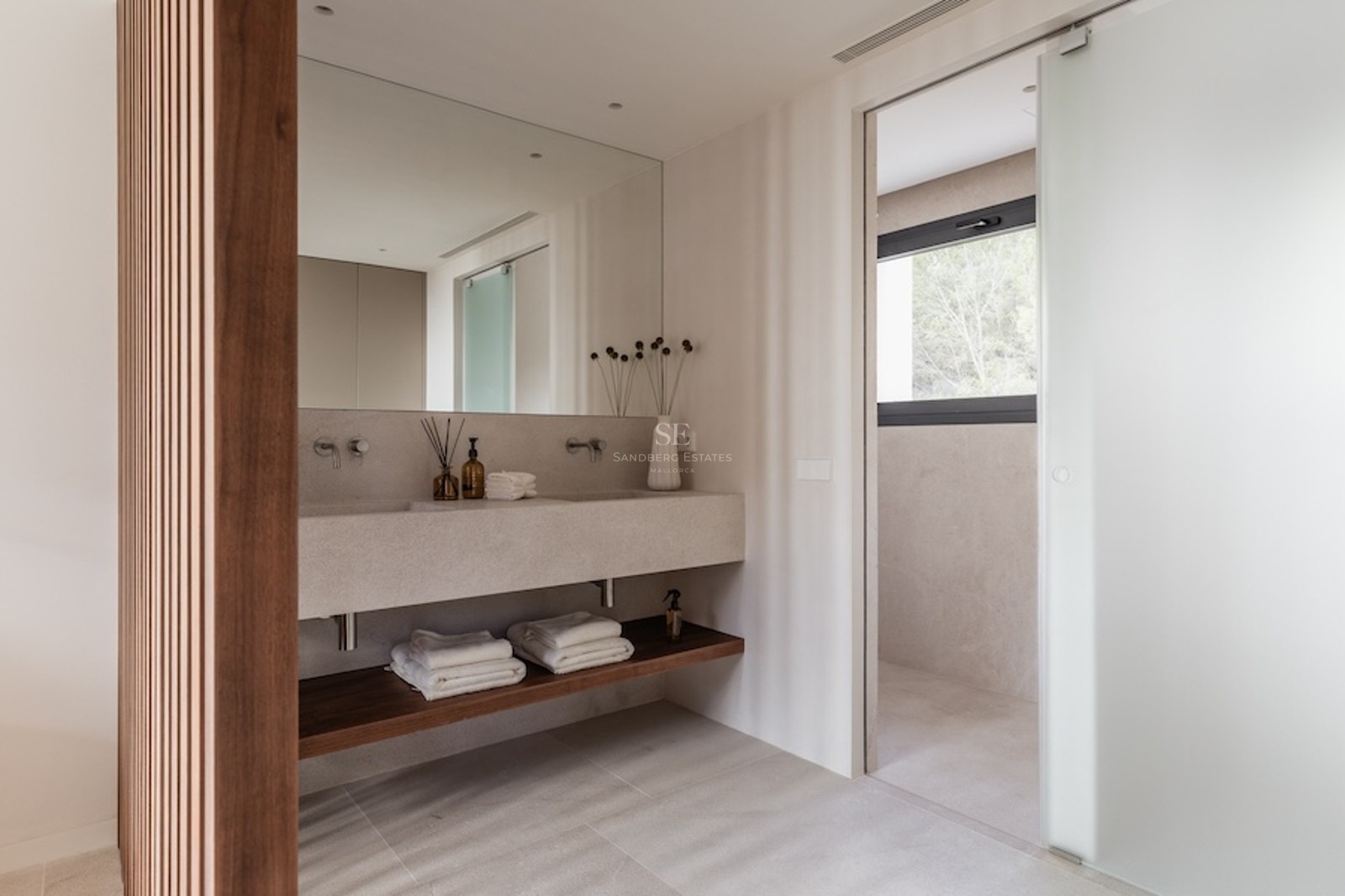 Modernes Master-Badezimmer mit beigem Steinwaschbecken, Holzlamellenwand und satinierter Glastür.