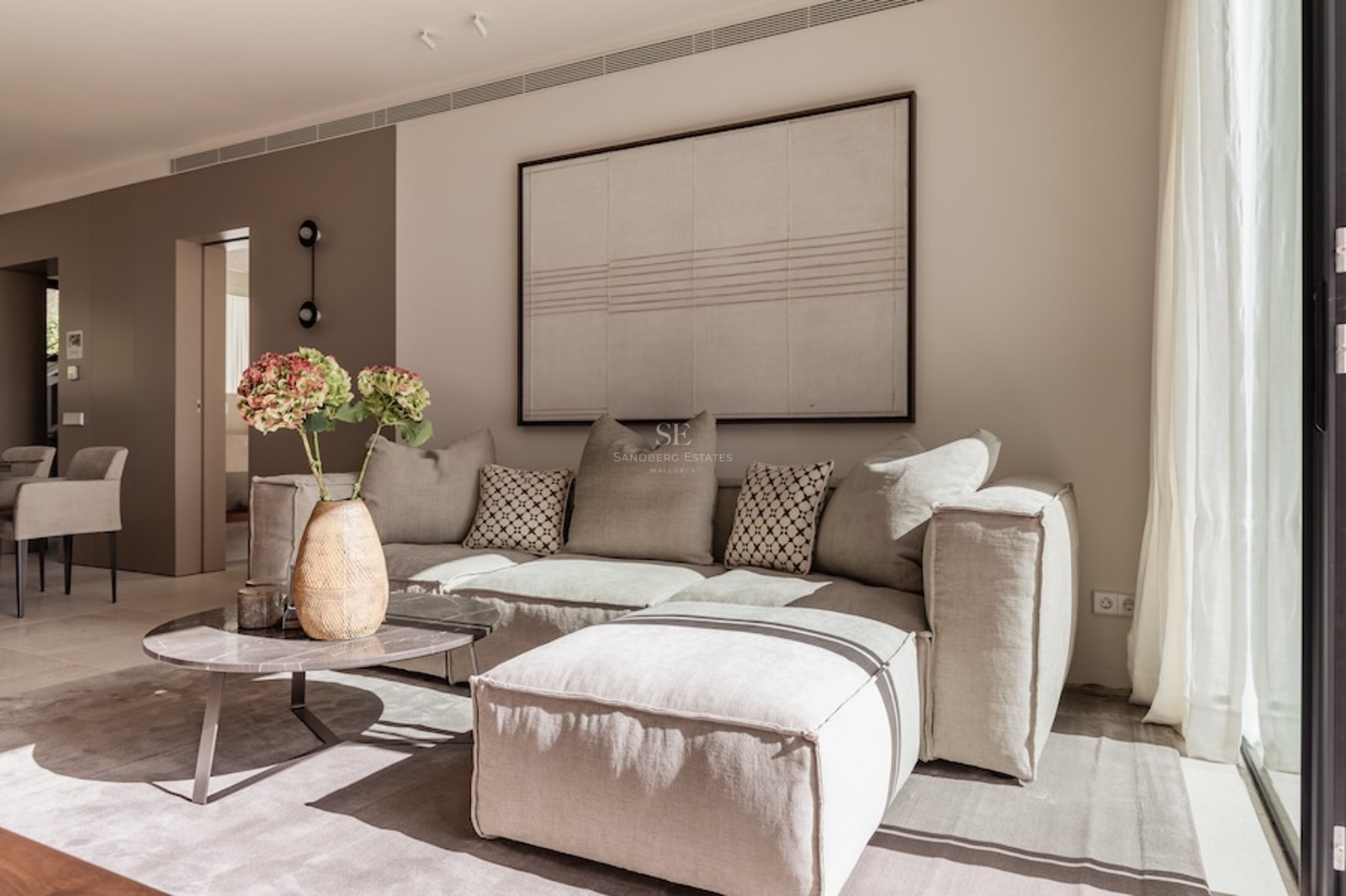 Minimalistisches Wohnzimmer mit einem großen beigen Ecksofa, Marmor-Couchtisch und großem abstrakten Wandbild.