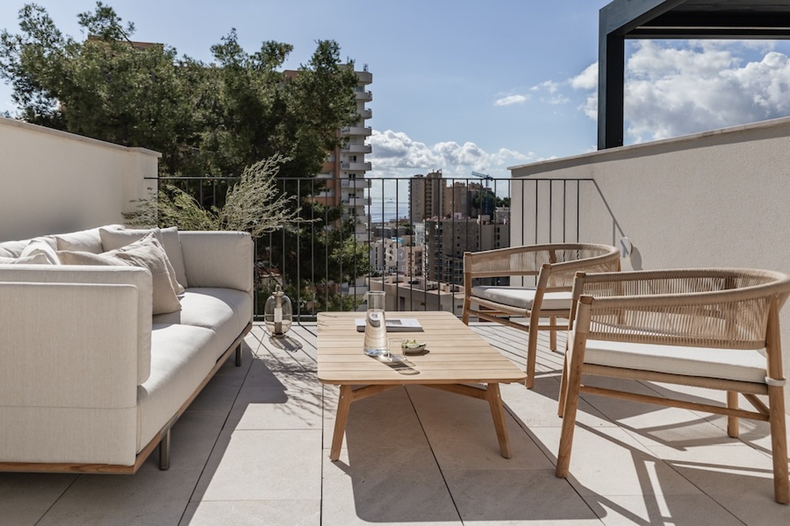 Luxuriöse Dachterrasse mit cremefarbenem Sofa, Holzsitzbänken und Blick auf die Stadt und das Meer unter blauem Himmel.